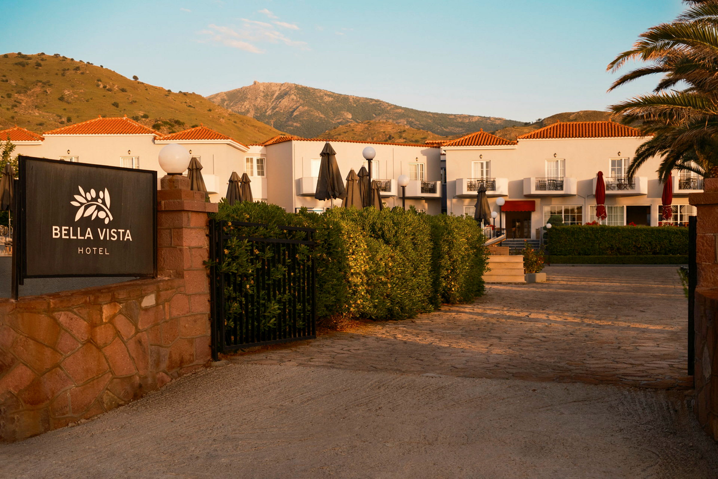 Hotellet Bella Vista med hvid facade og røde tage, beliggende ved en bjergskråning. (AI-genereret tekst)