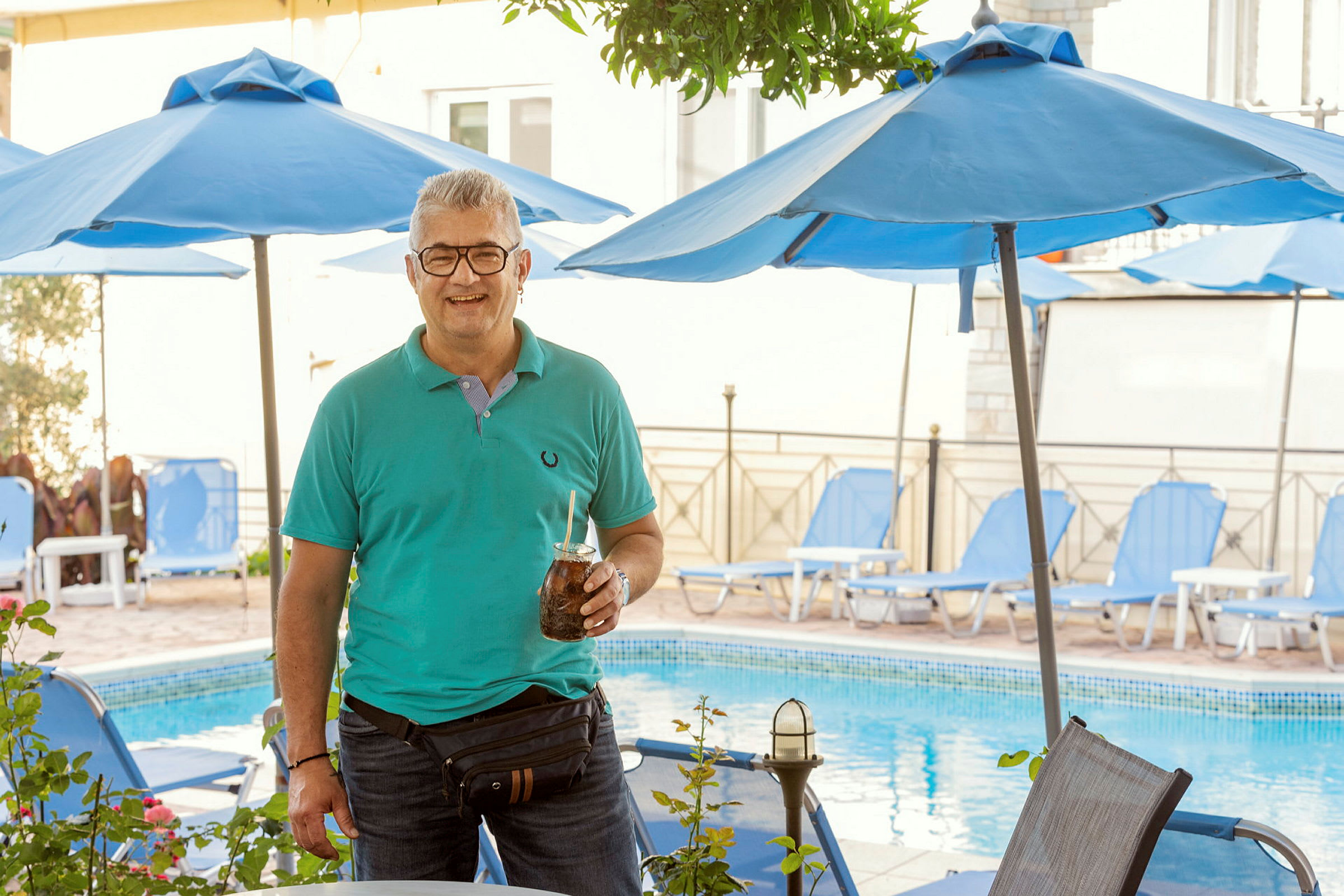 Personen står foran en pool. Baggrunden viser liggestole og parasoller. (AI-genereret tekst)