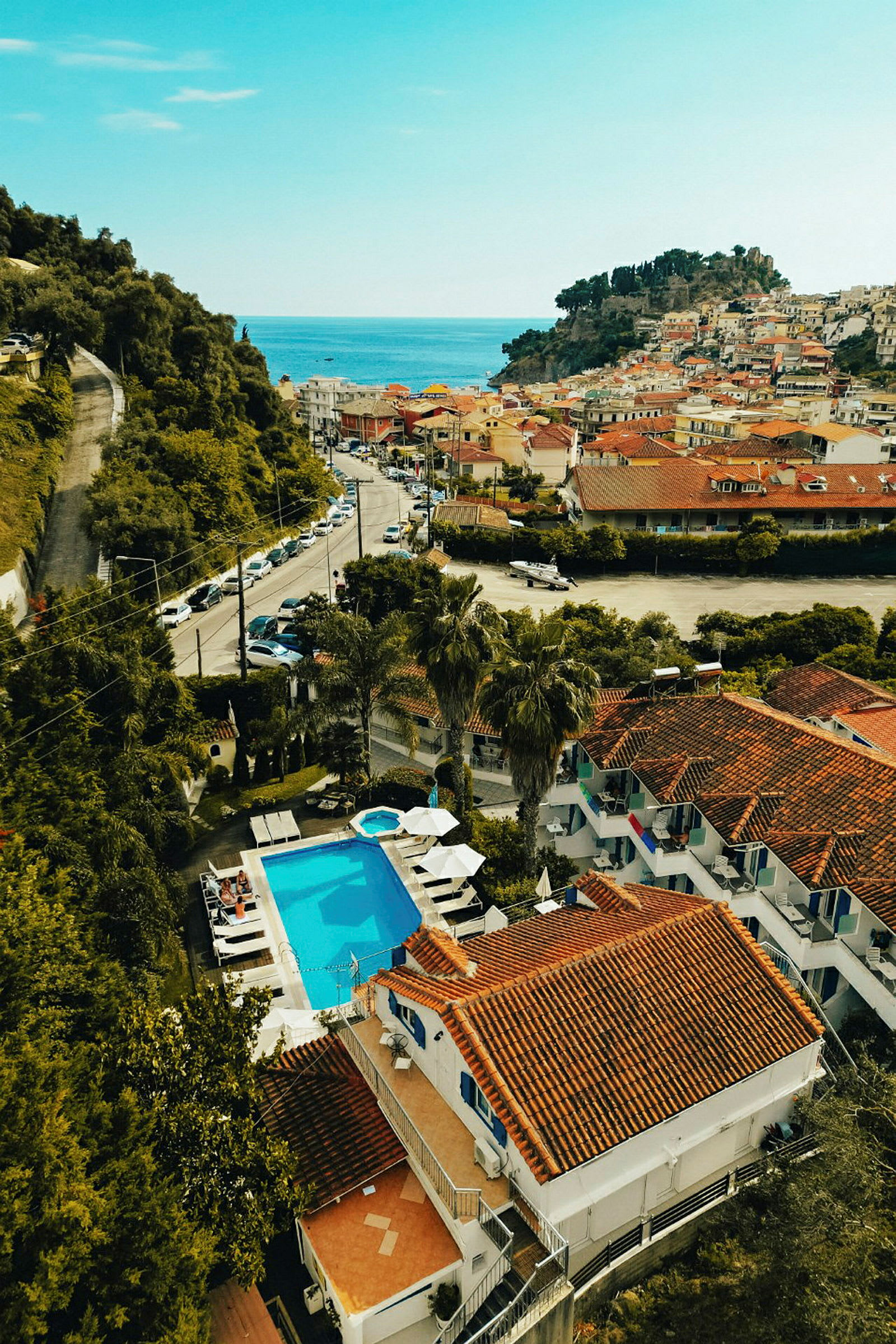 Udsigt over en lille by med røde tage, pool og havet i baggrunden. (AI-genereret tekst)