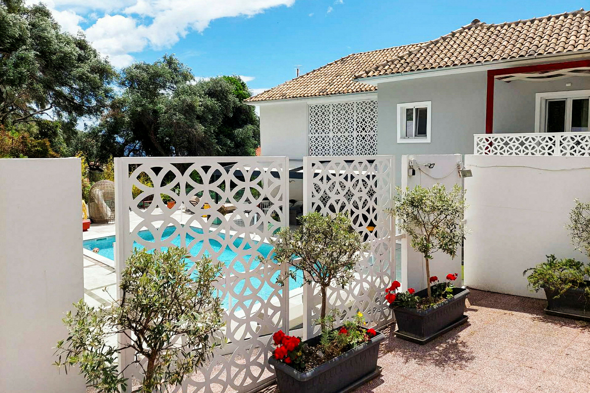 En villa med en pool og dekorative hvide skærme foran, omgivet af planter og blomster. (AI-genereret tekst)