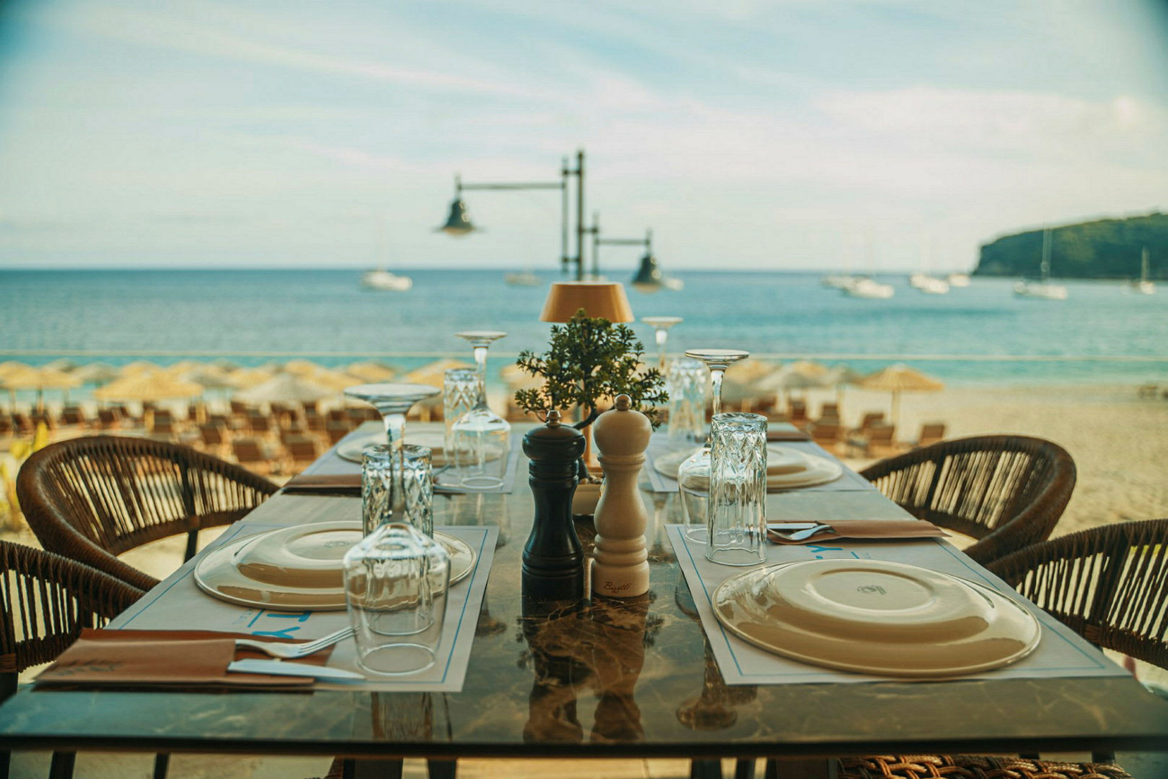 Et dækket bord på en restaurant ved stranden med havet i baggrunden. (AI-genereret tekst)