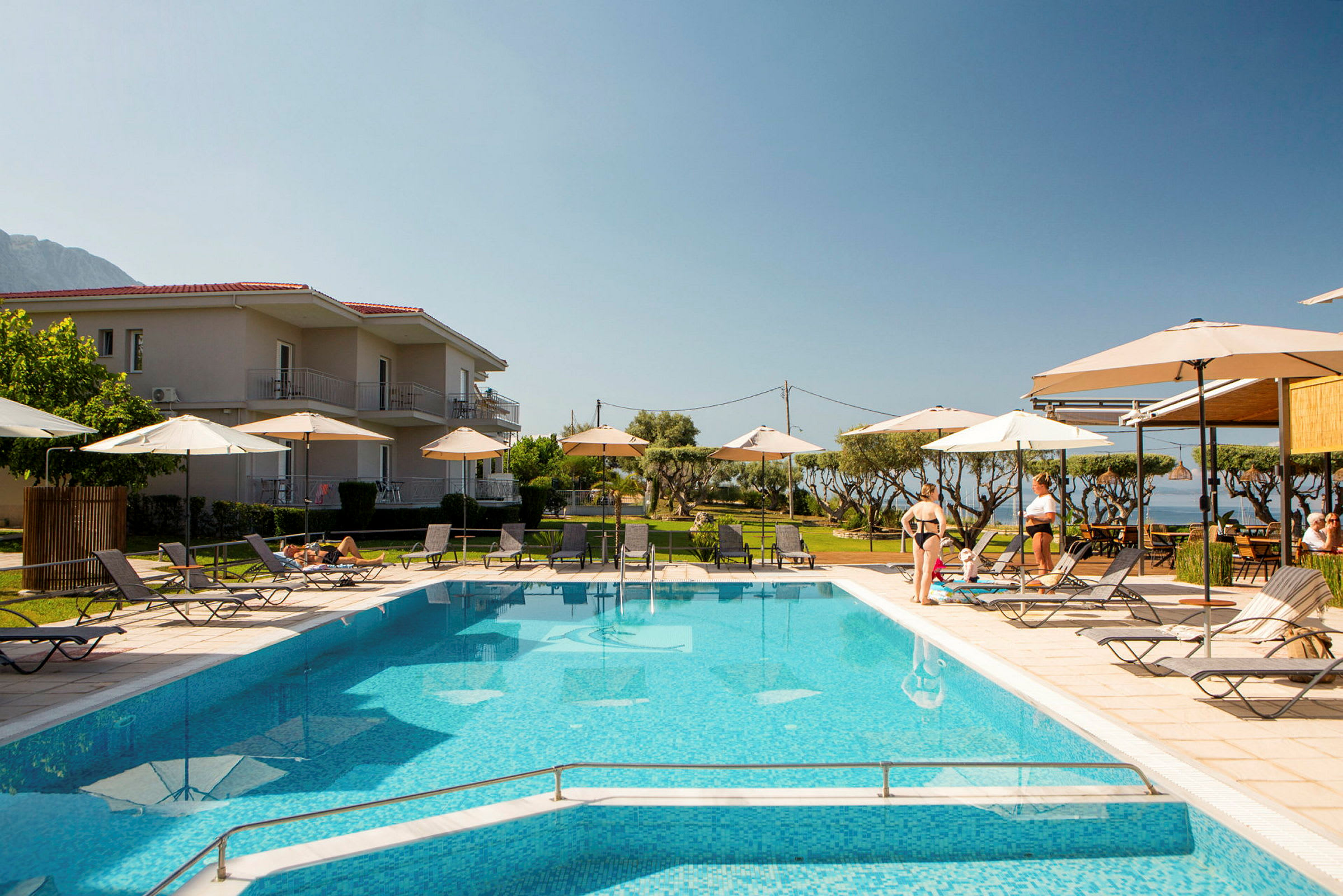 Hotelområde med udendørs pool, liggestole og parasoller. (AI-genereret tekst)