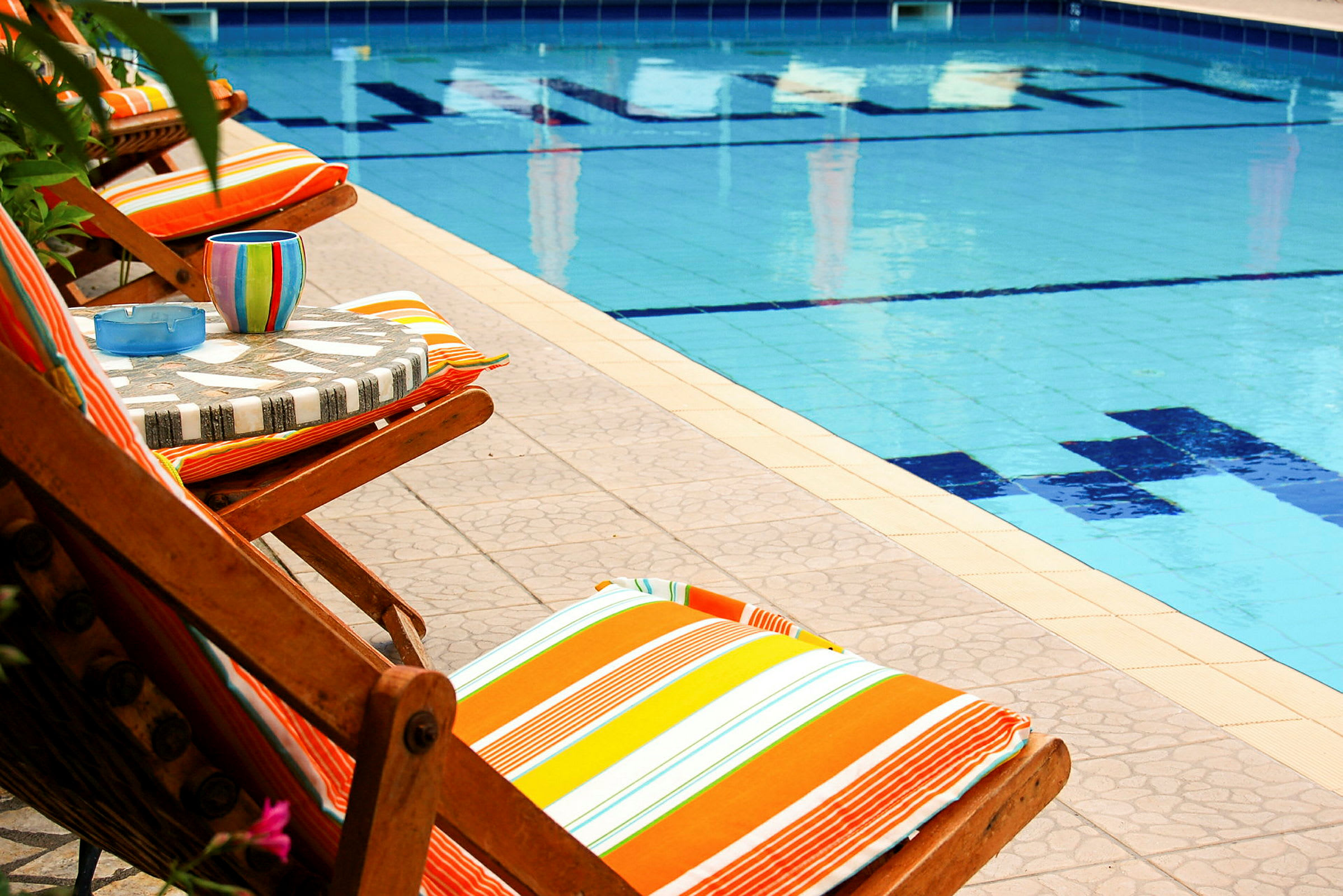 Liggestole med farverige puder ved kanten af en swimmingpool. (AI-genereret tekst)