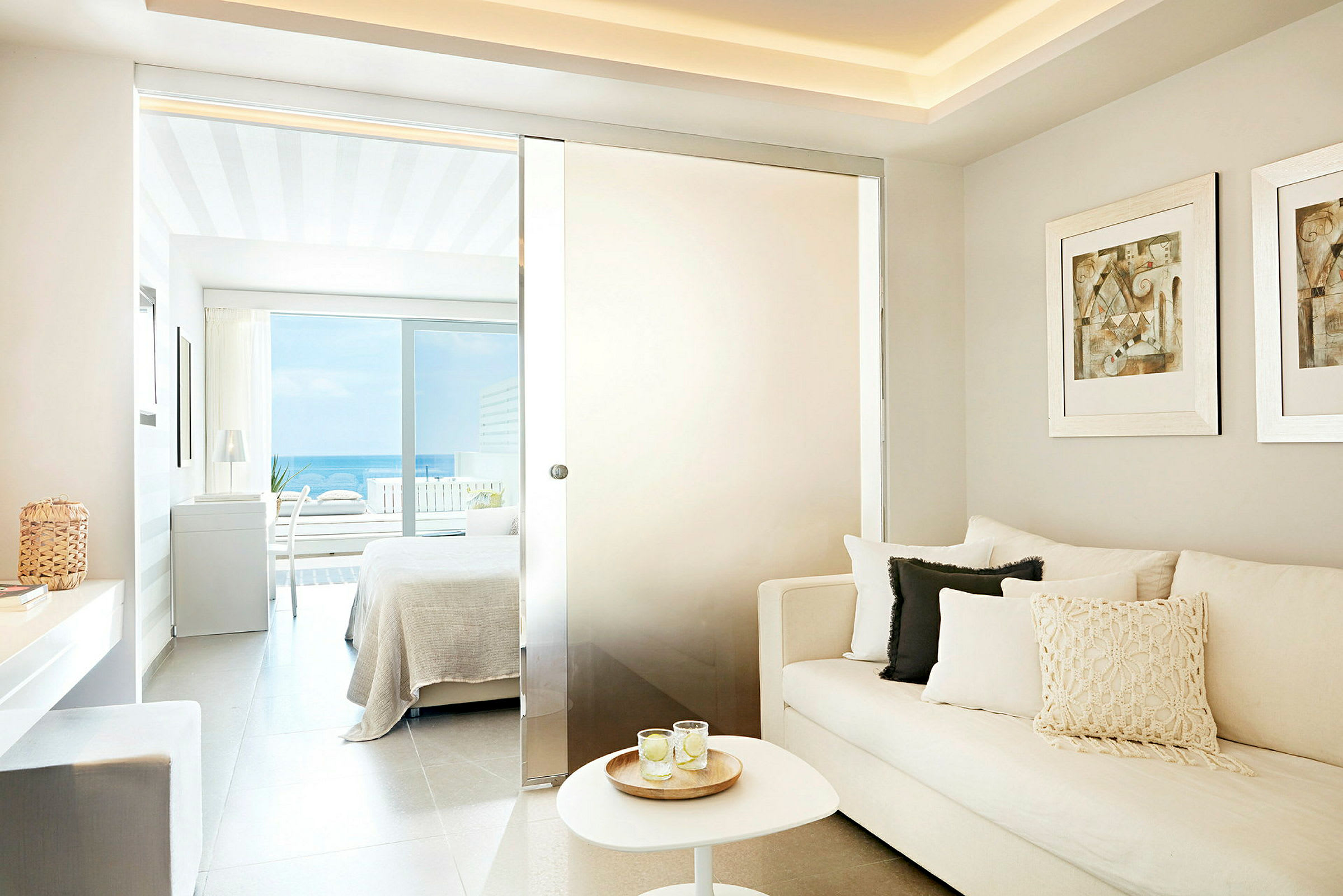 Et moderne hotelværelse med sofa og seng tæt på en balkon med havudsigt. (AI-genereret tekst)