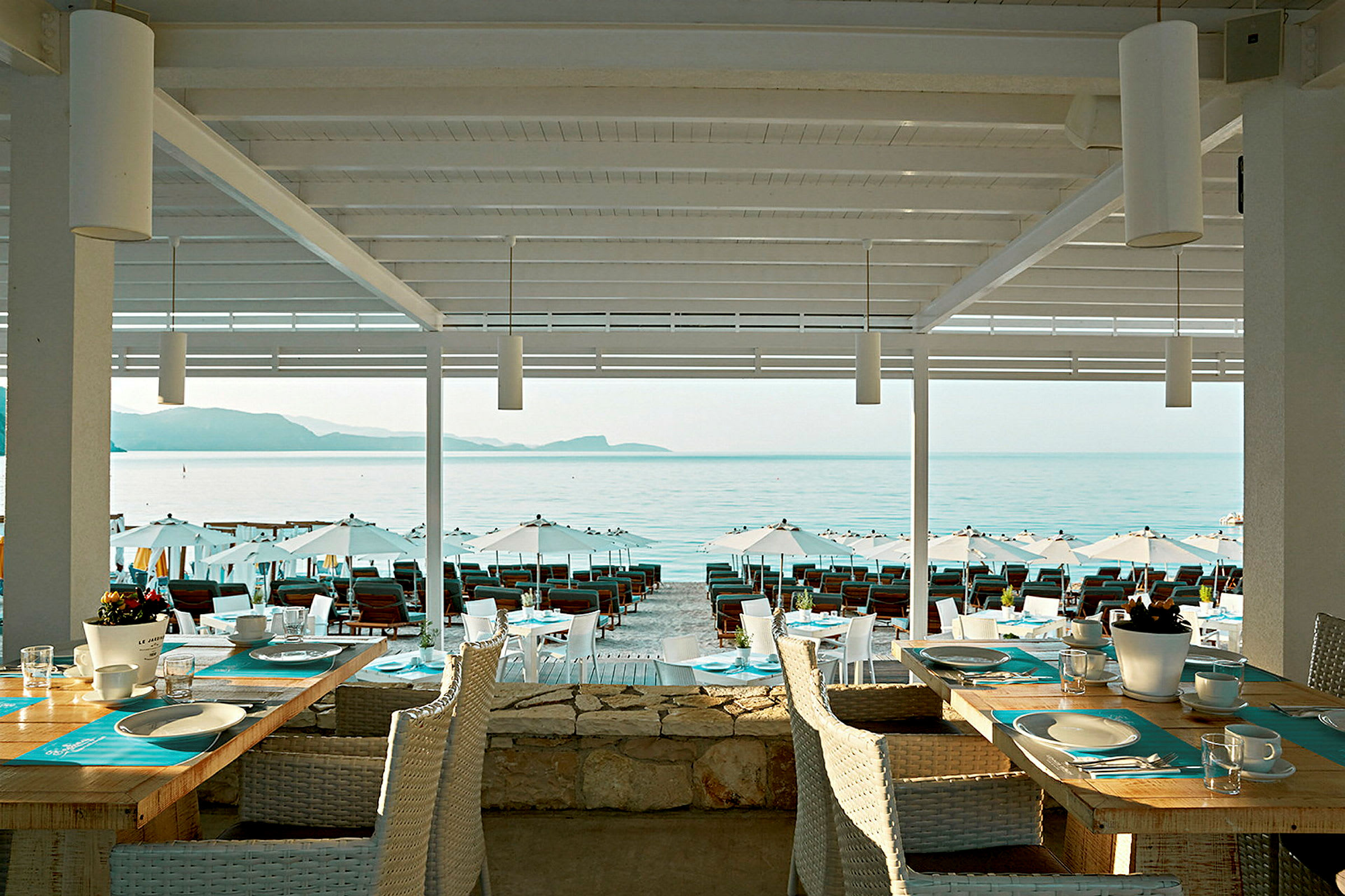 Udsigt fra en restaurant med dækkede borde mod stranden og havet. (AI-genereret tekst)