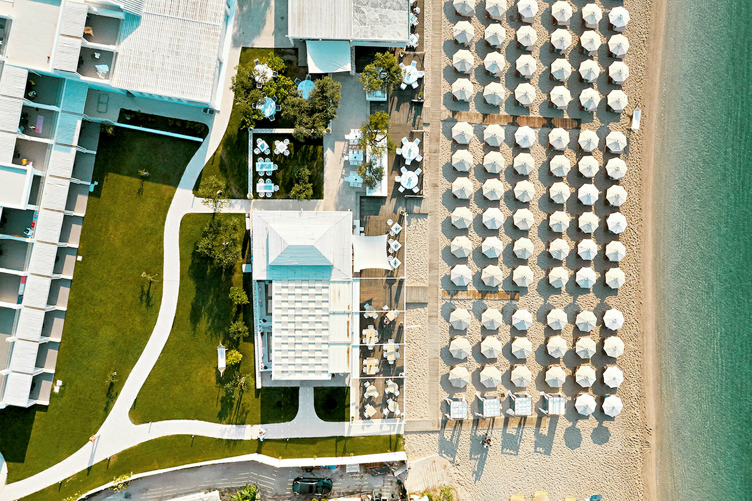 Luftfoto af hotelbygning med græsplæner og strand med parasoller. (AI-genereret tekst)