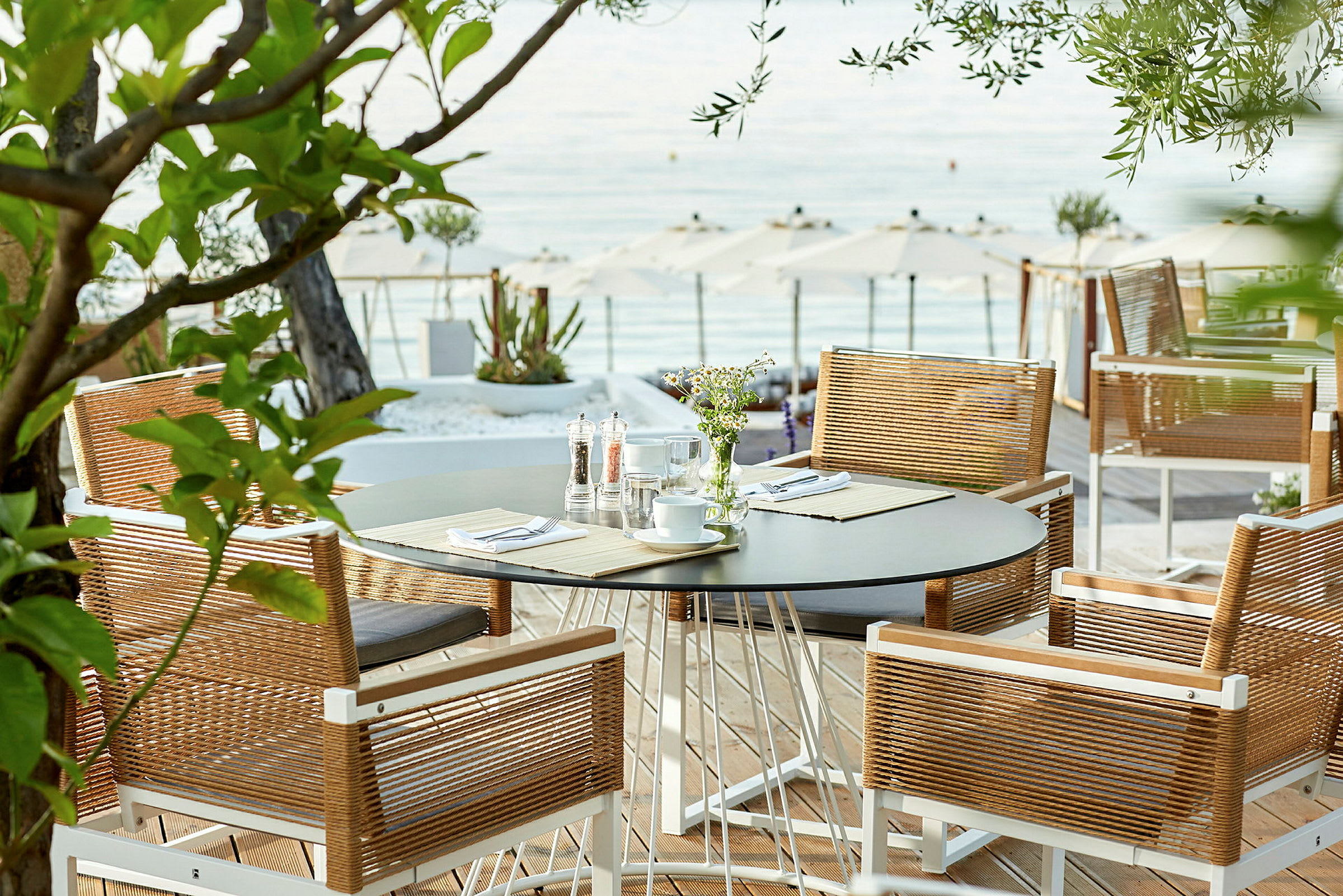 Udsigt mod et bord med stole på en terrasse nær havet. (AI-genereret tekst)