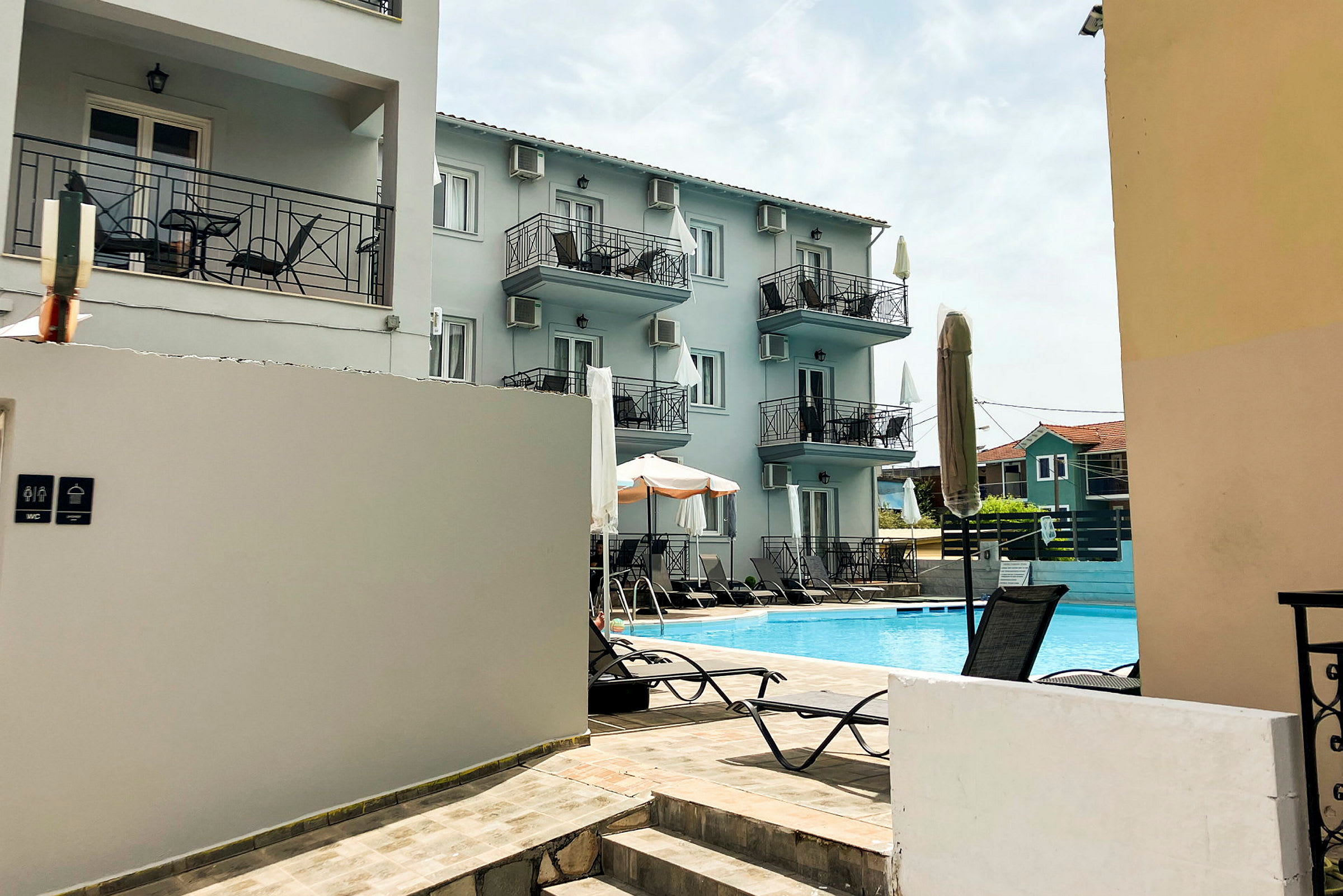 Hotelbygning med altaner og en pool foran. (AI-genereret tekst)
