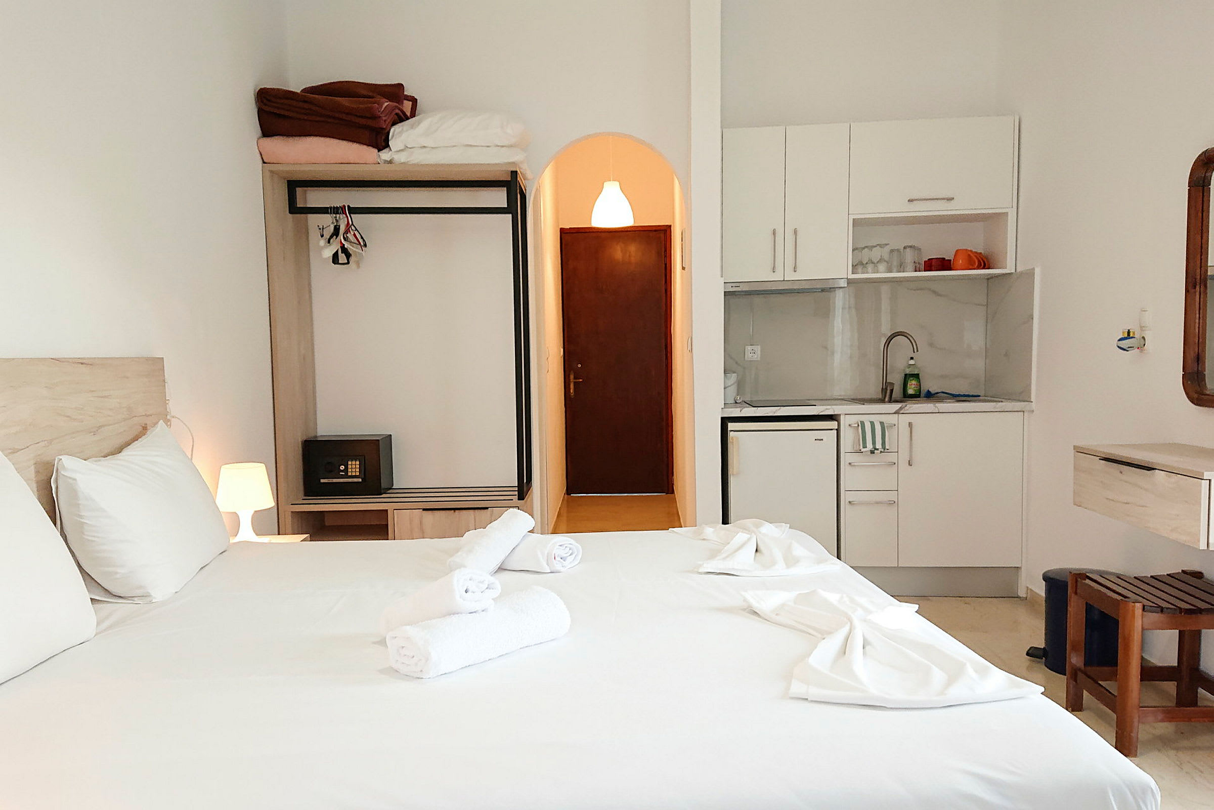 Hotelværelse med en redt dobbeltseng, garderobe, dør, tekøkken og stol. (AI-genereret tekst)