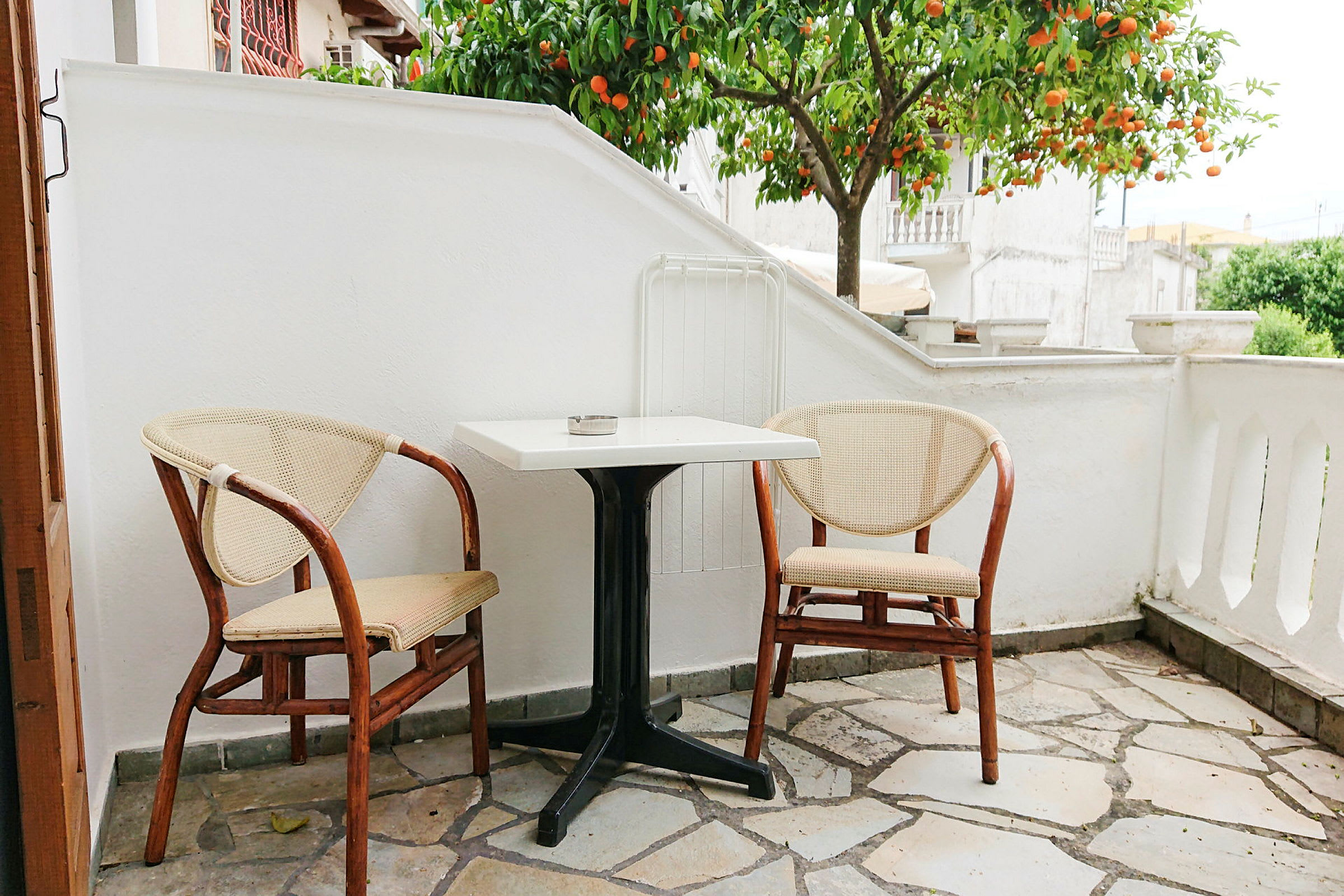 En lille terrasse med to stole og et bord foran et appelsintræ. (AI-genereret tekst)