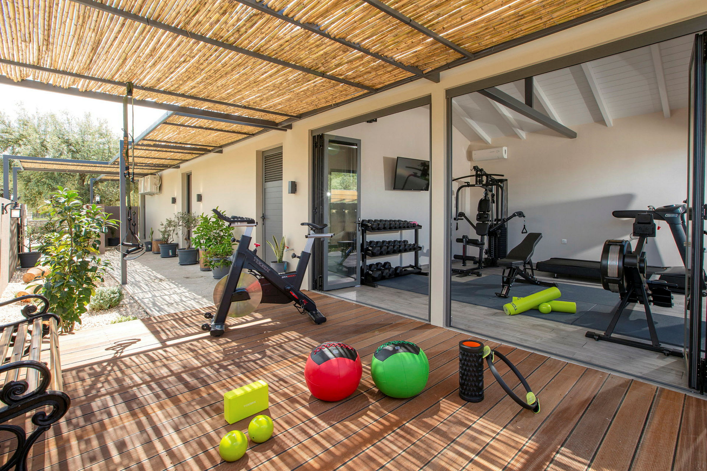 Et fitnesscenter med udstyr og træningsredskaber ved en terrasse med planter. (AI-genereret tekst)