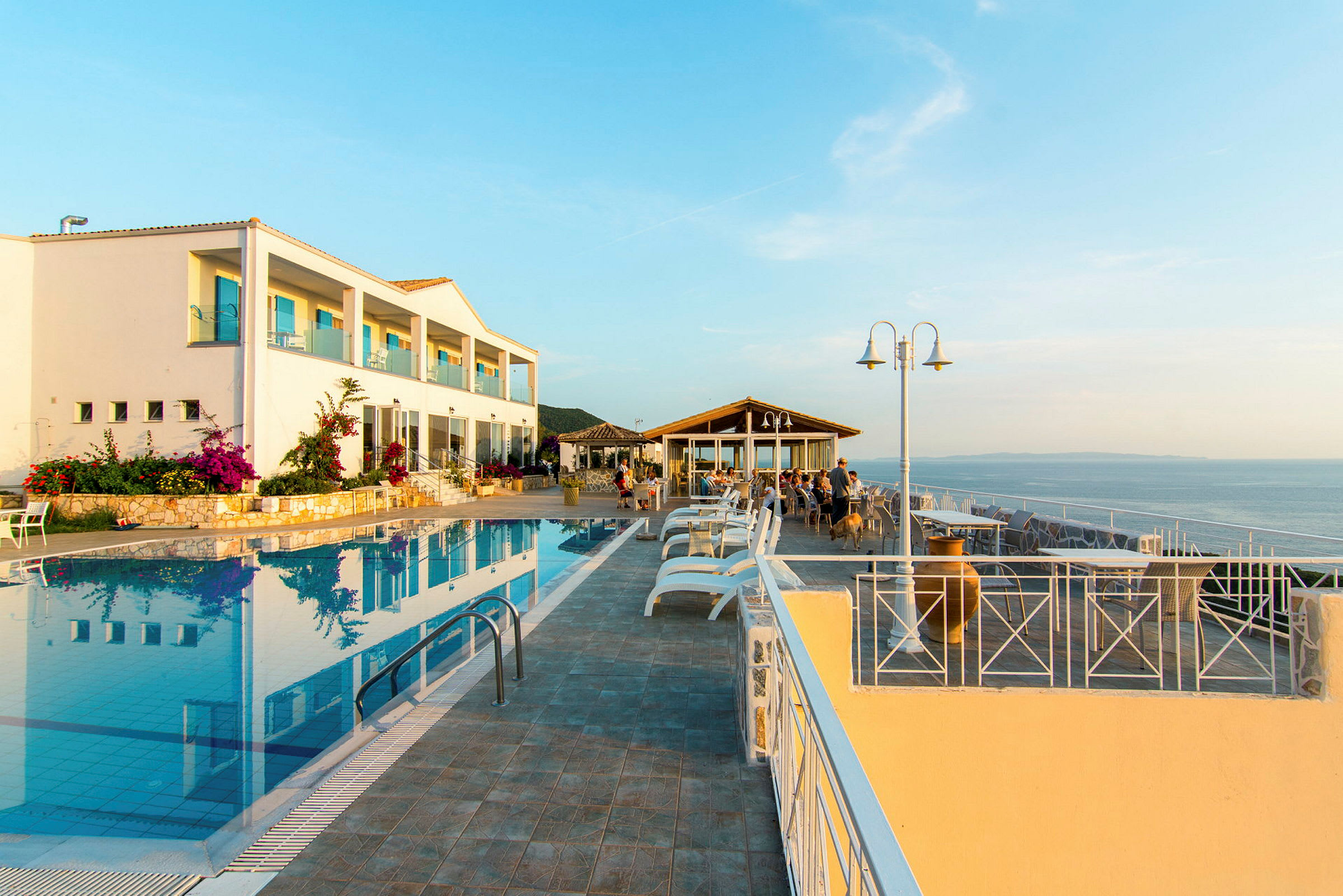 En hotelbygning ved en udendørs pool og en siddegruppe med udsigt over havet. (AI-genereret tekst)