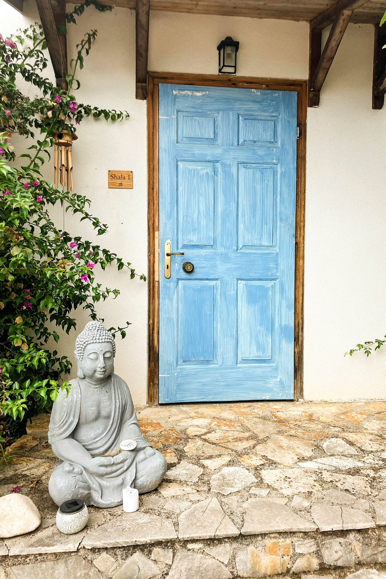 En blåtmalet dør med en stenstatue af en siddende Buddha foran. (AI-genereret tekst)