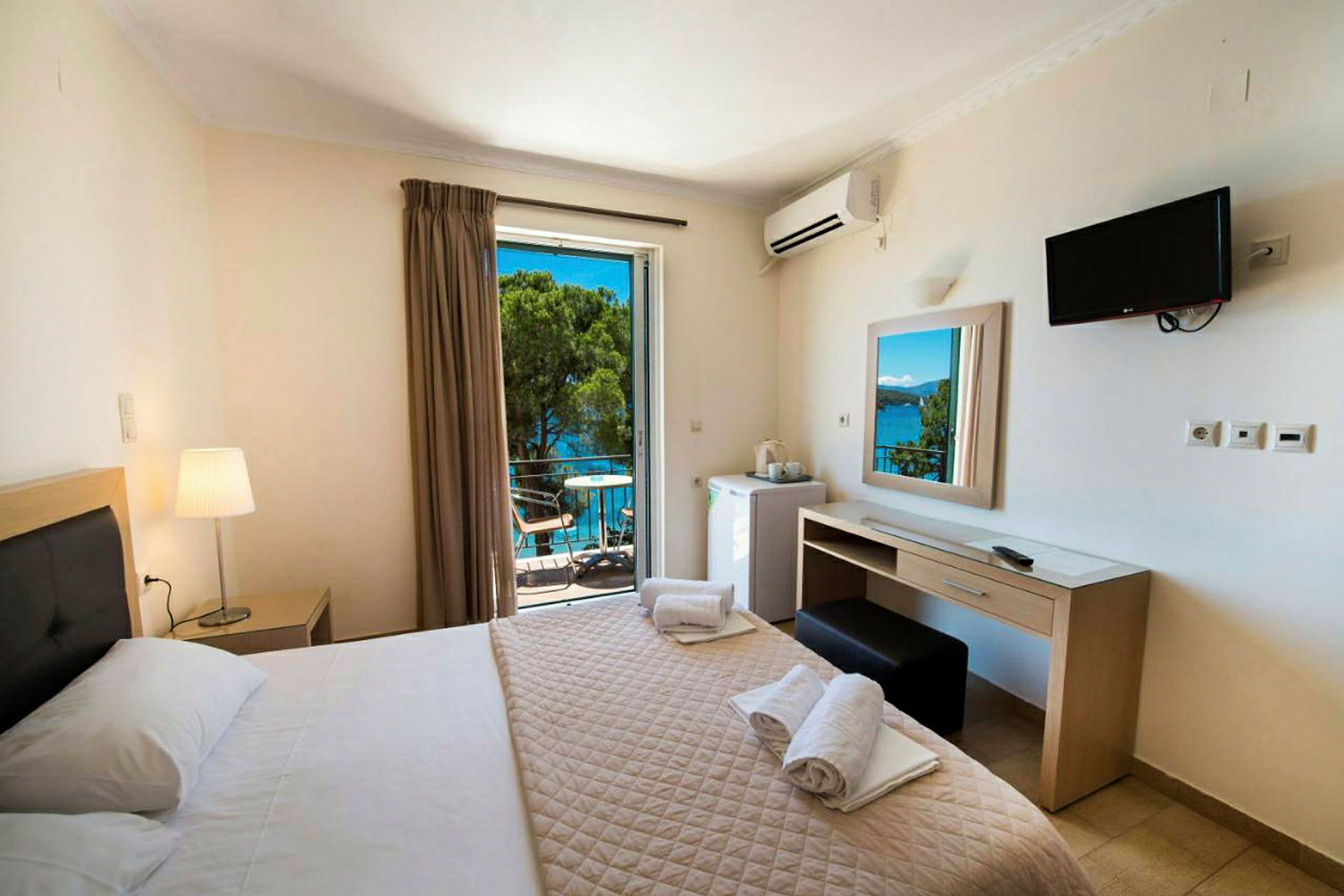 Hotelværelse med dobbeltseng, skrivebord, TV og balkon med udsigt over havet. (AI-genereret tekst)