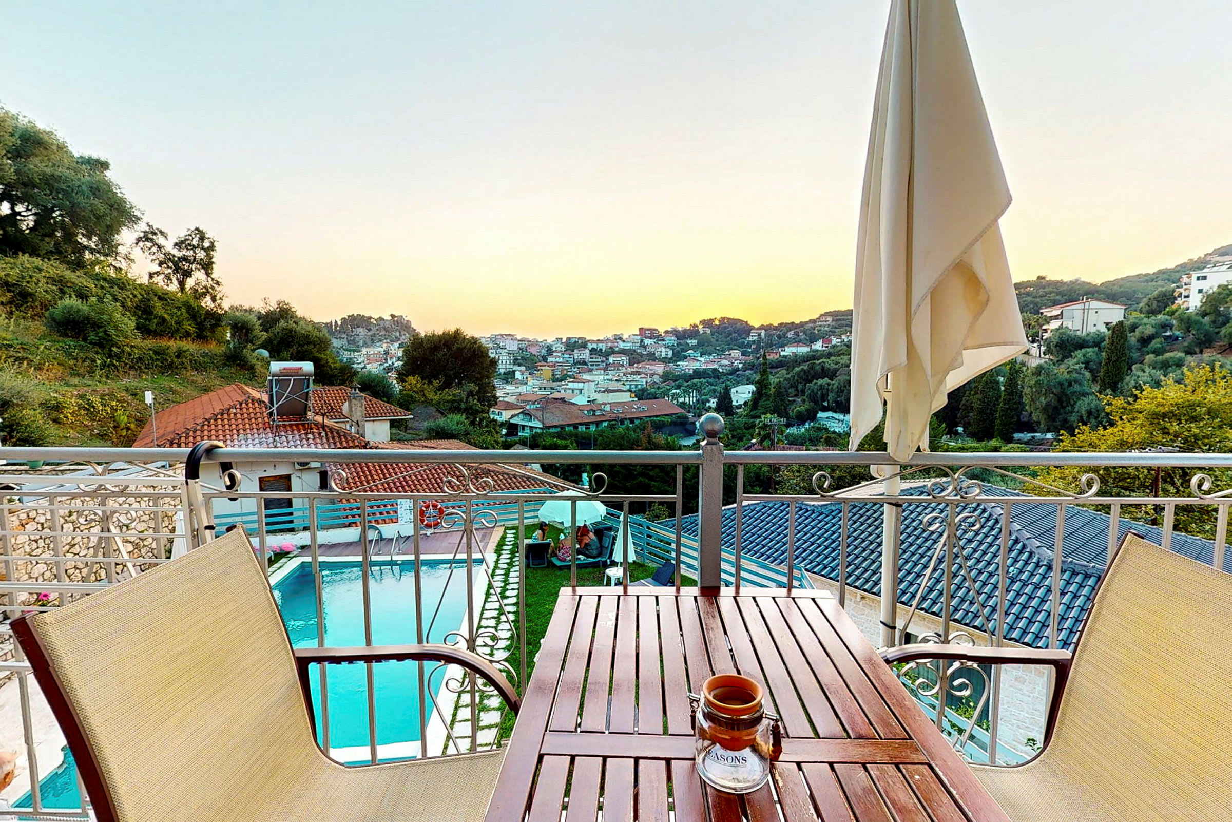 Udsigt fra en balkon med et bord og stole, en pool og byen i baggrunden. (AI-genereret tekst)