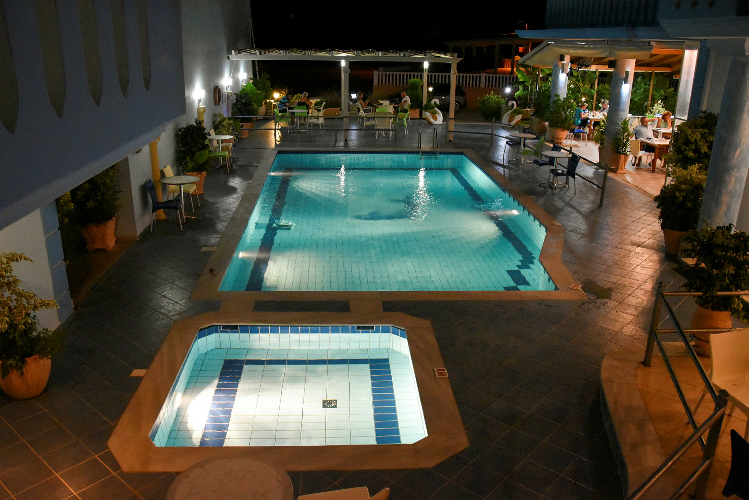 Udendørs pool med omkringliggende siddepladser og belysning om aftenen. (AI-genereret tekst)