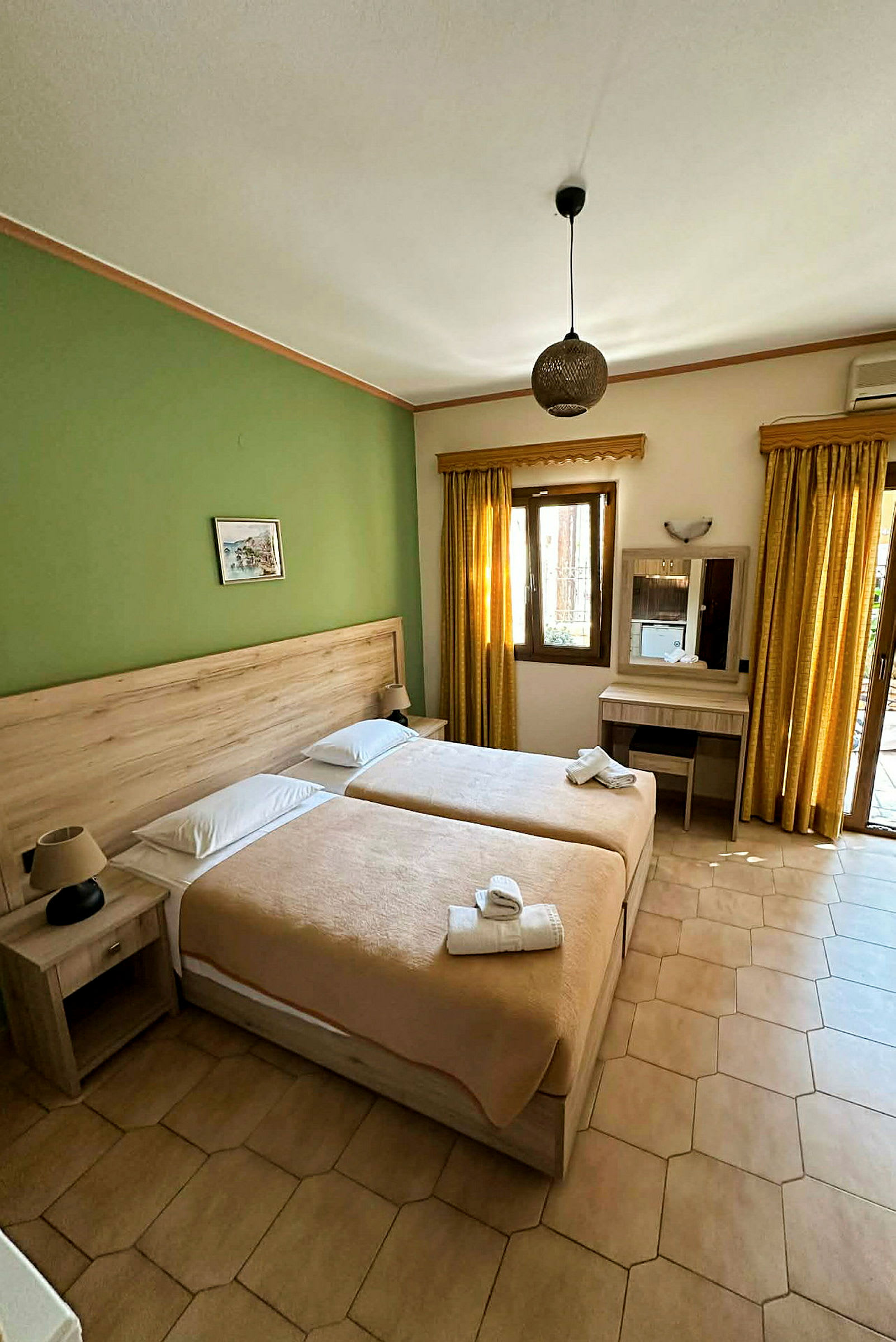 Hotelværelse med to enkeltsenge, grøn væg, beige sengetøj og møbler, samt vindue med gule gardiner. (AI-genereret tekst)