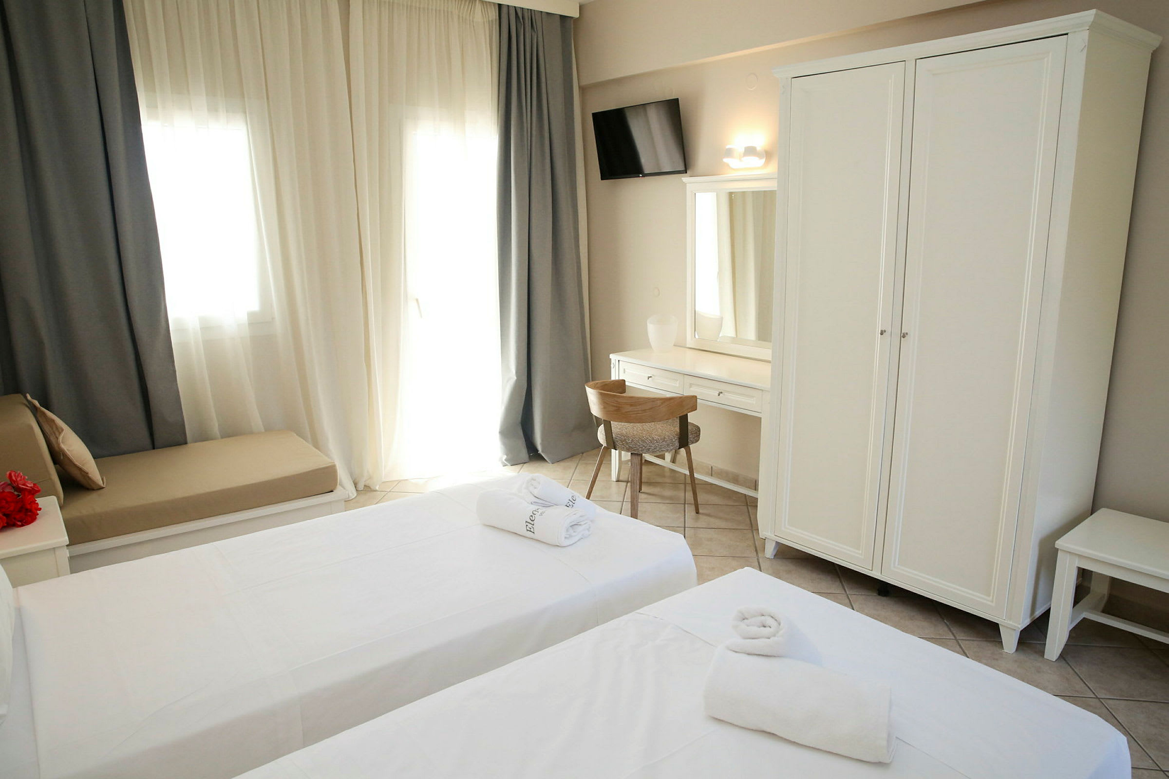 Billede af et hotelværelse med to senge, hvid garderobe og skrivebord. (AI-genereret tekst)
