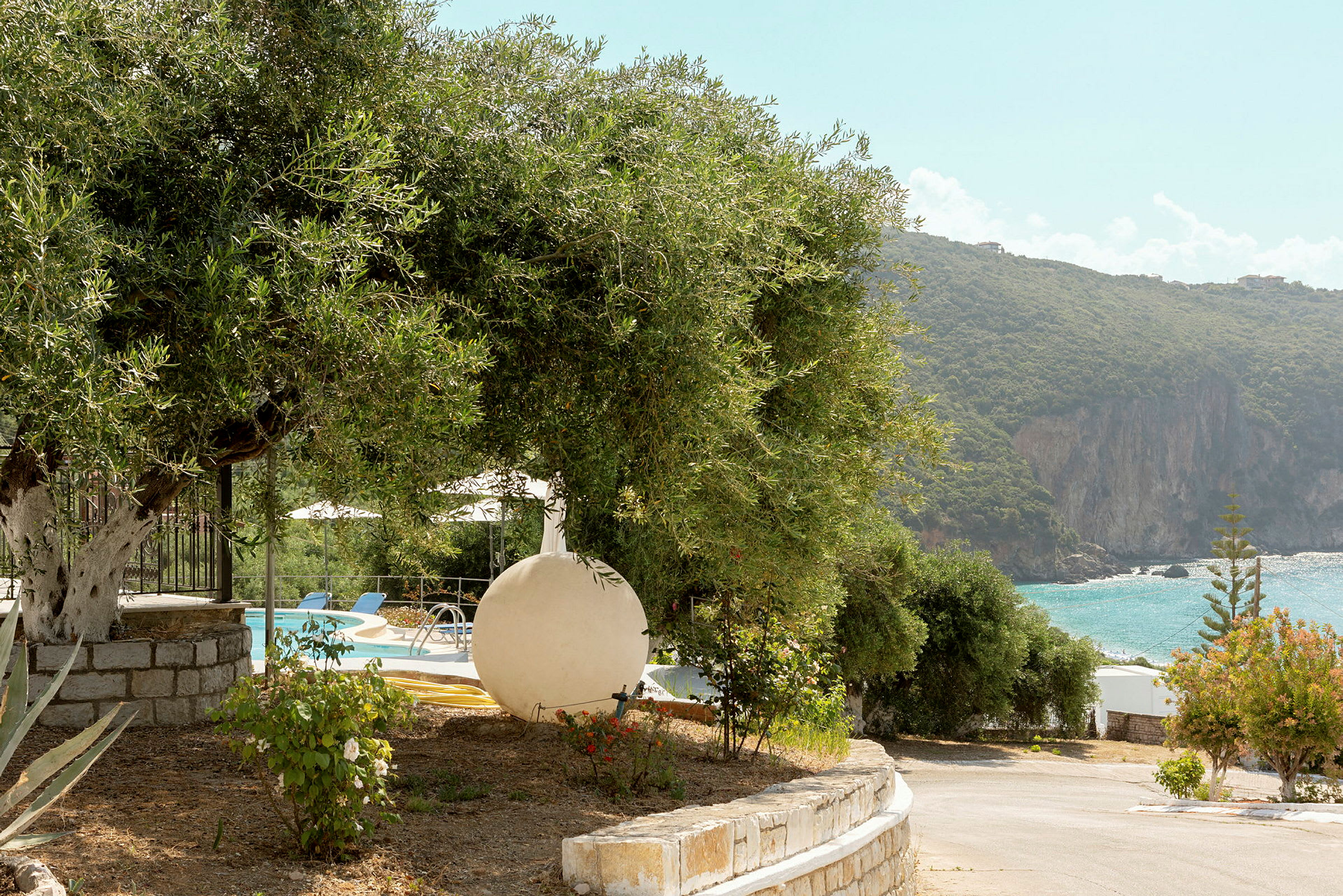 Udsigt over en pool omgivet af vegetation og en strand med klipper ved havet. (AI-genereret tekst)