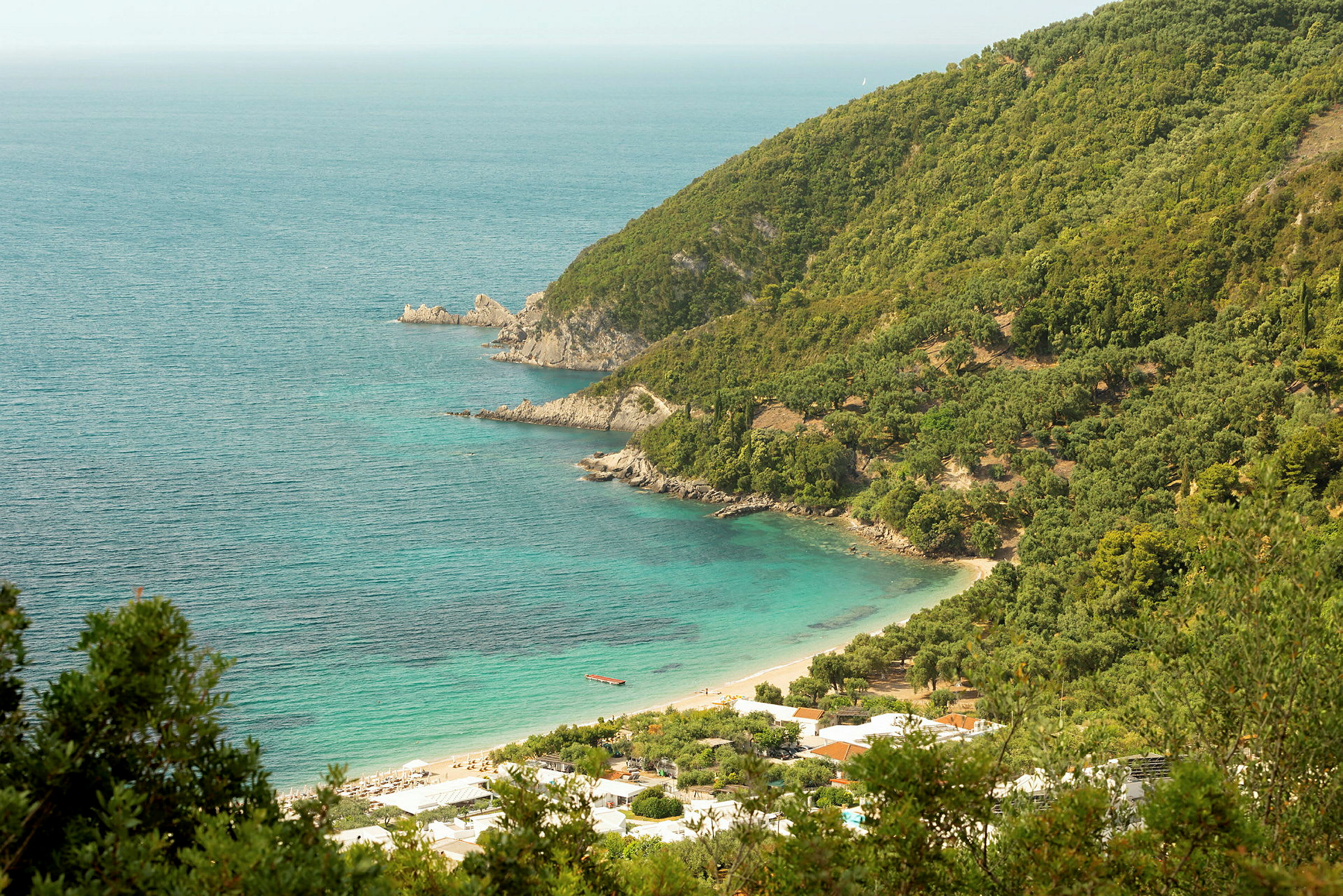 En kystlinje med frodige klipper og en strand ved turkis vand. (AI-genereret tekst)