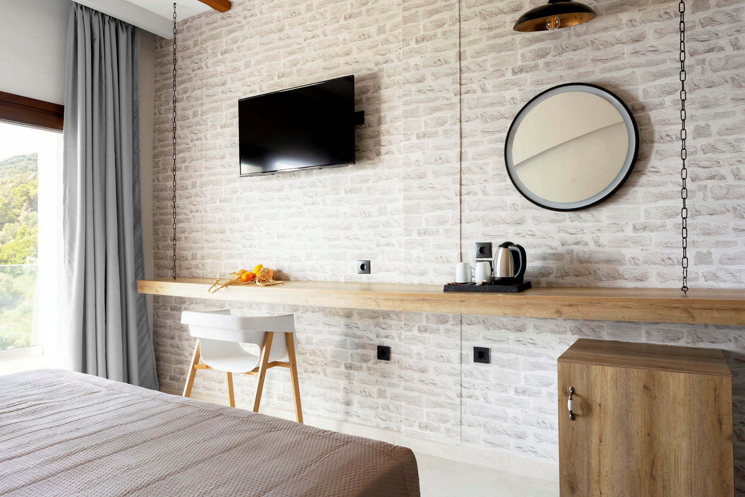 Et hotelværelse med en hvid murstensvæg, et moderne TV, et rundt spejl og bord med kaffemaskine. (AI-genereret tekst)