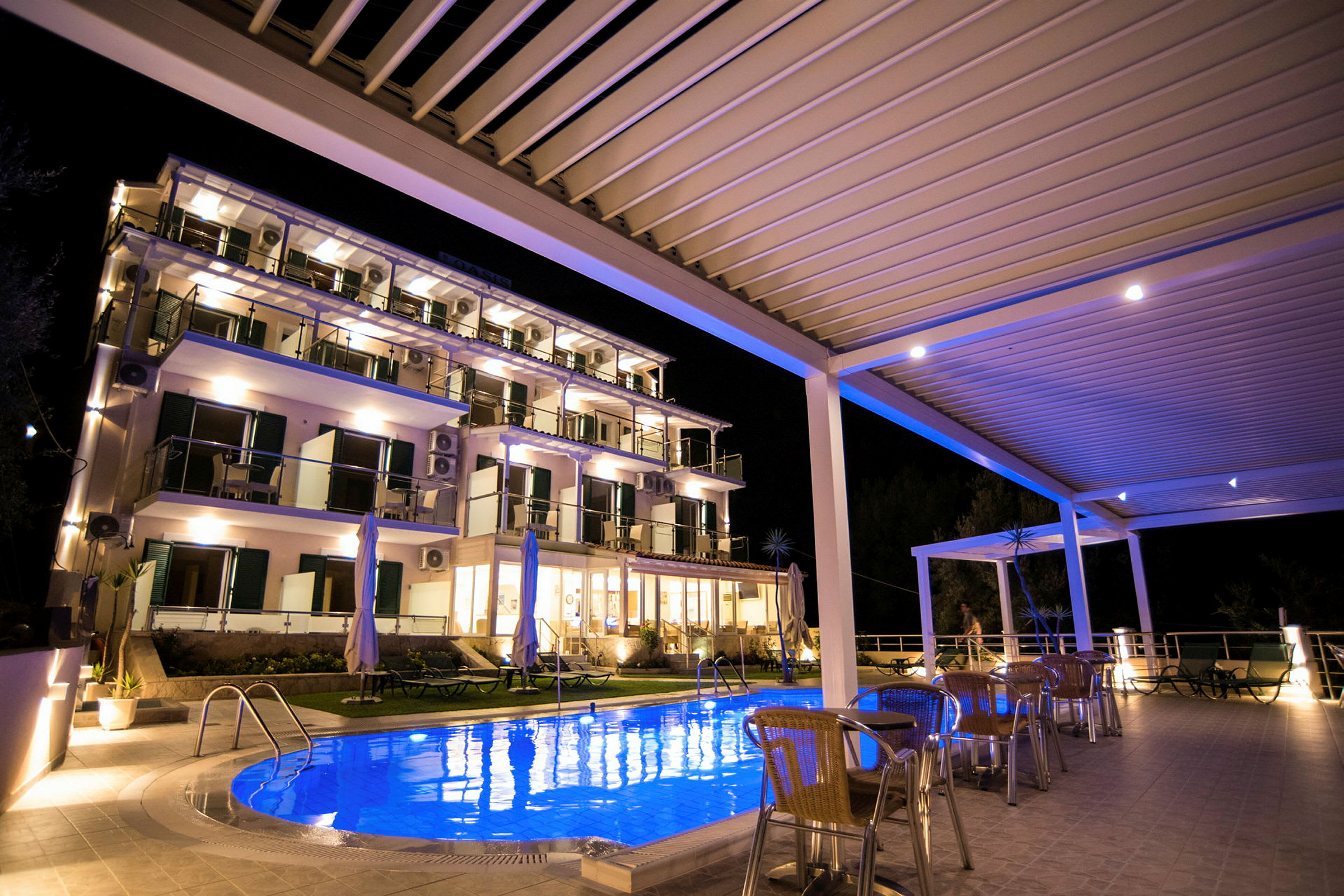 Et hotel med oplyst pool og udendørsmøbler om aftenen. (AI-genereret tekst)