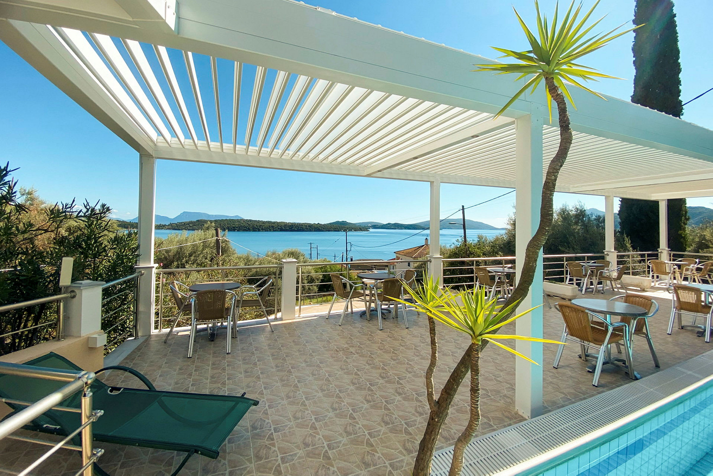 Terrasse med siddepladser under en hvid pergola, udsigt over havet og omgivelserne. (AI-genereret tekst)