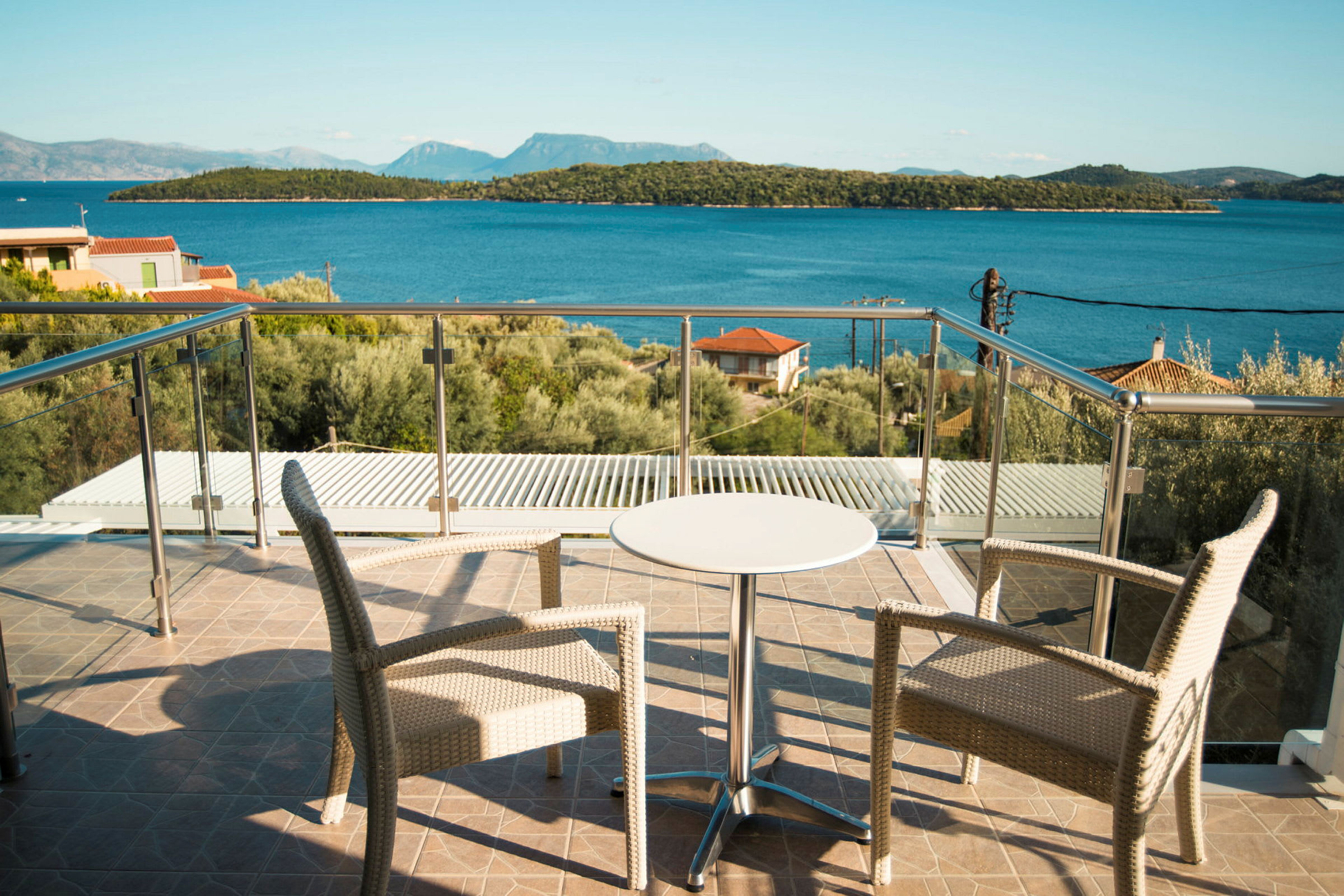 To stole og et lille bord på en terrasse med glasrækværk, udsigt til havet og skovklædte øer. (AI-genereret tekst)