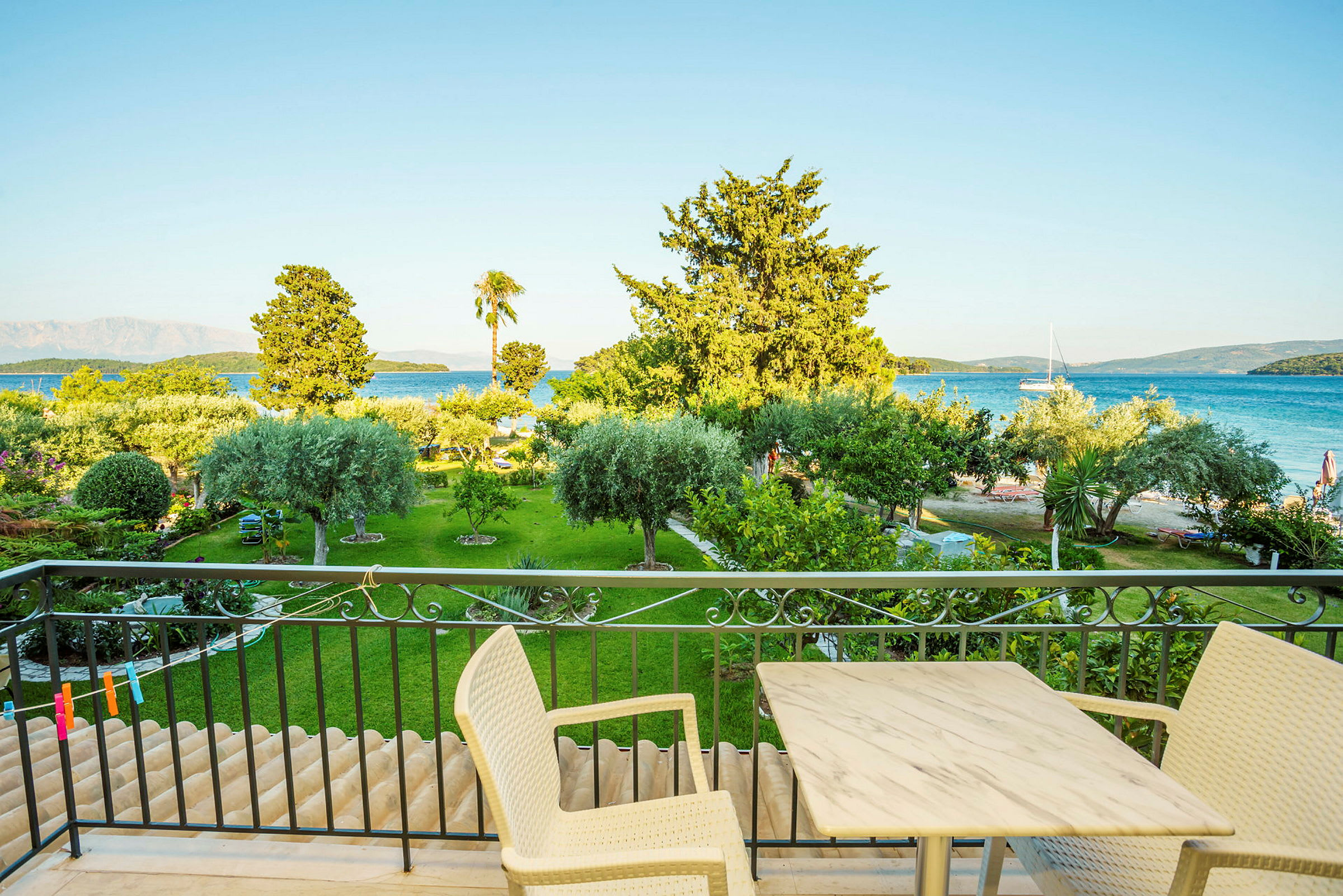 Udsigt fra en balkon mod en frodig have og en strand med havet i baggrunden. (AI-genereret tekst)
