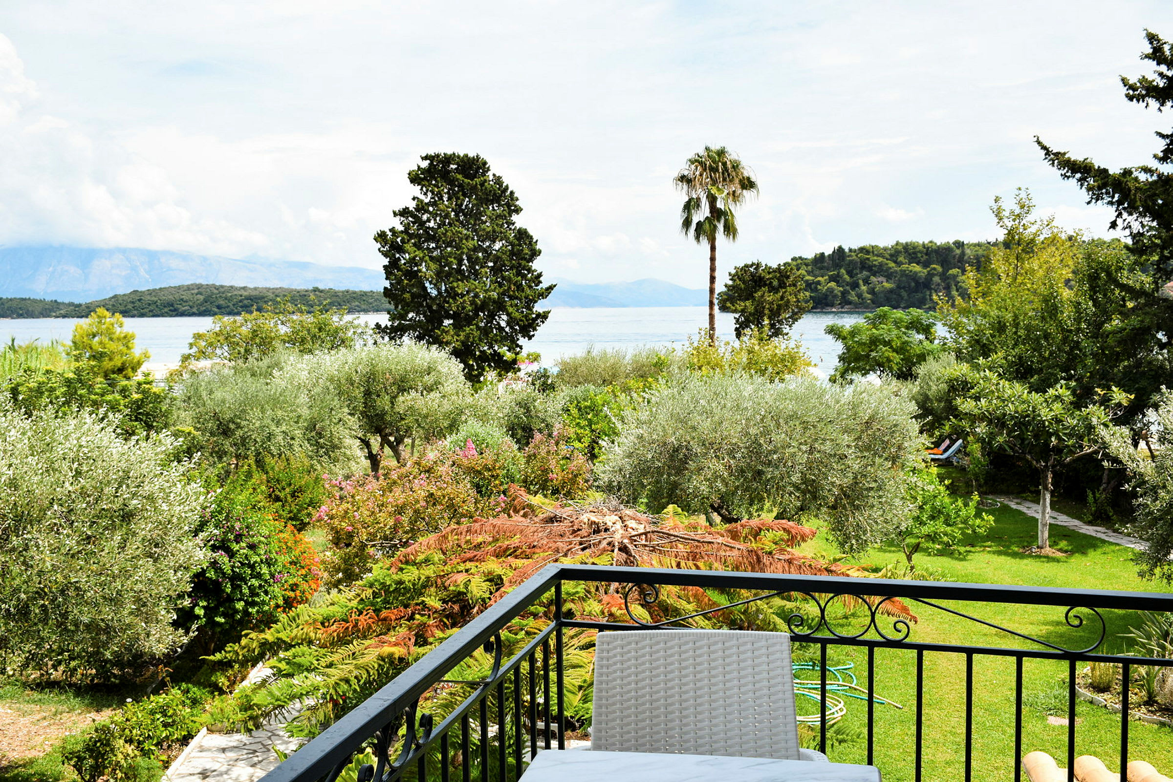 Udsigt fra en balkon mod en have og havet i baggrunden. (AI-genereret tekst)