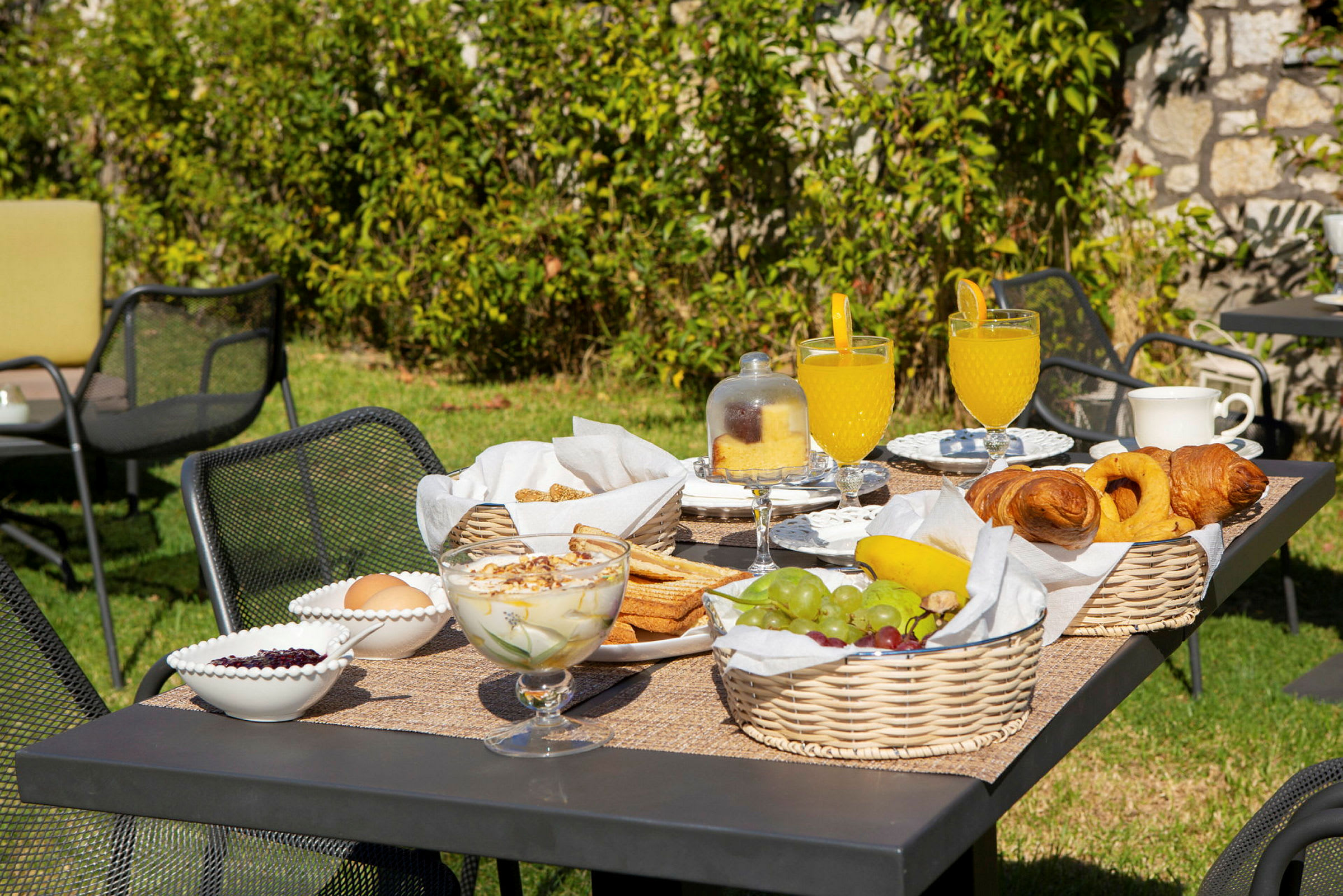 Havebord med morgenmad, der indeholder frugt, bagværk og drikke. (AI-genereret tekst)