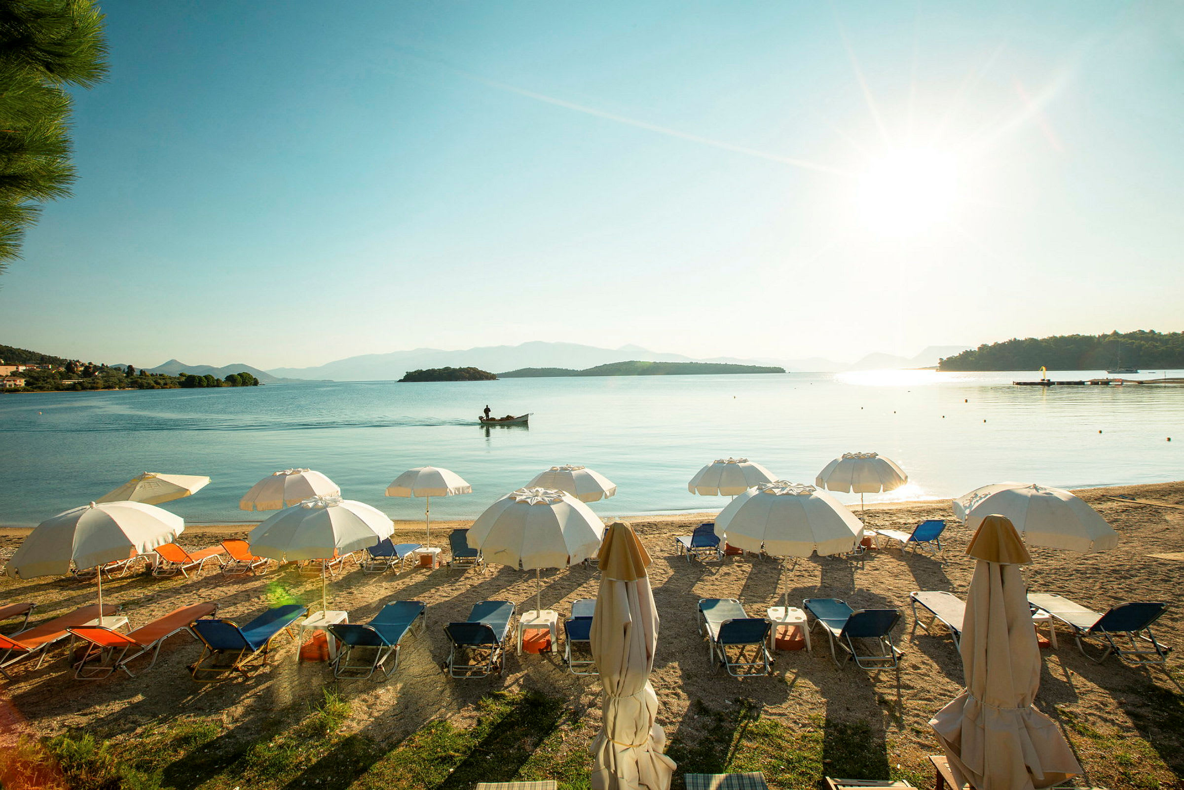 Strand med liggestole og parasoller, med havet og små øer i baggrunden under en klar himmel. (AI-genereret tekst)