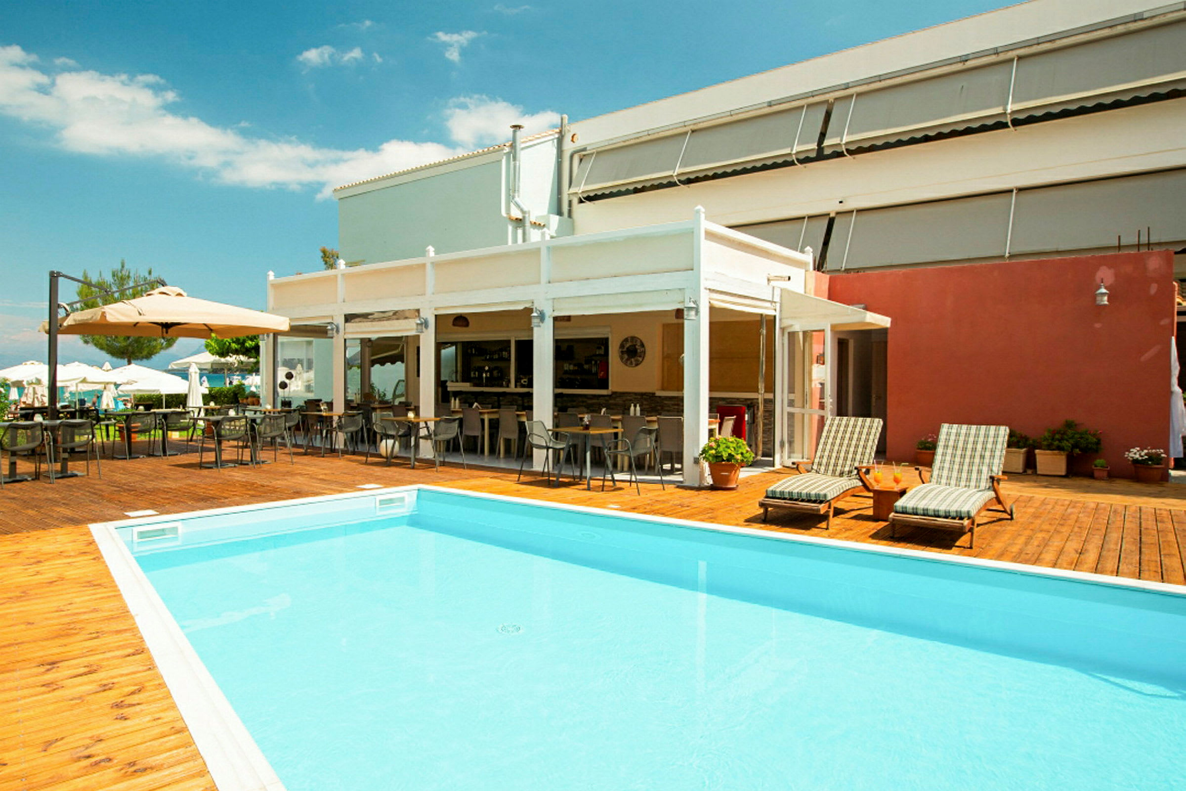 Udendørs område med pool, liggestole og udendørs servering ved et hotel. (AI-genereret tekst)