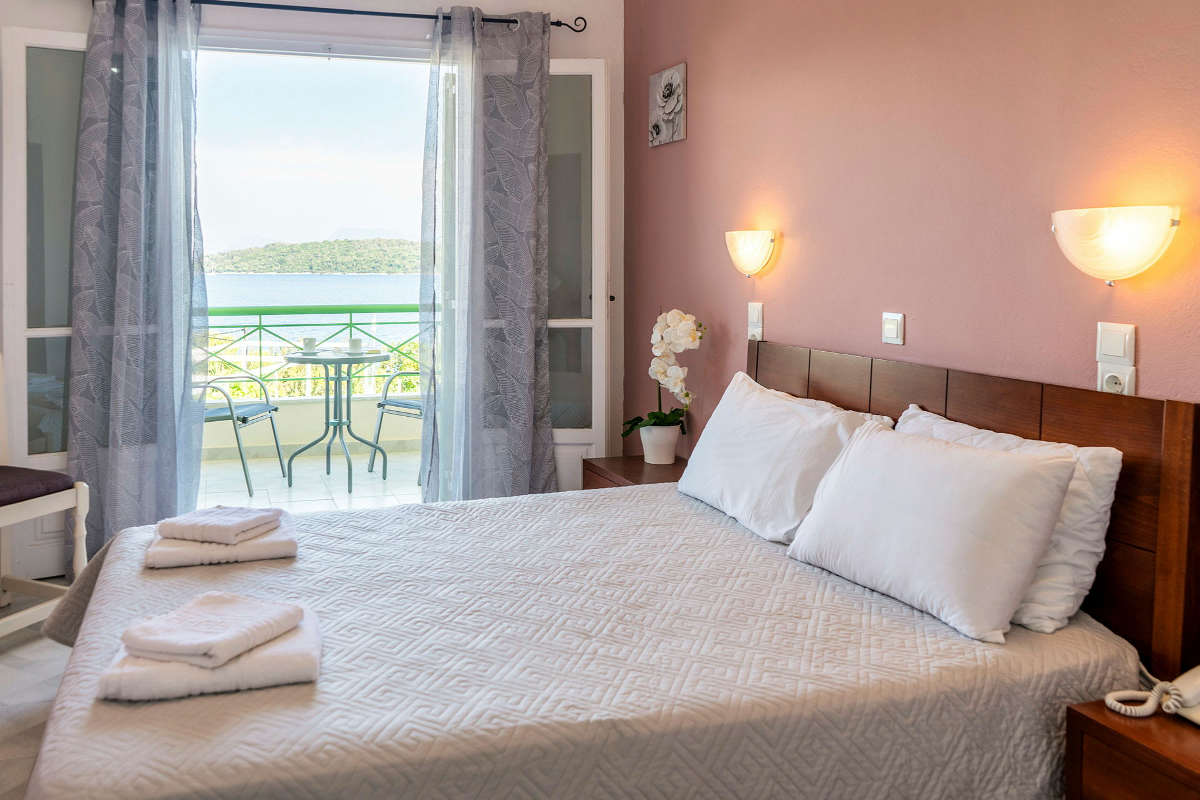 Et hotelværelse med en dobbeltseng, håndklæder på sengen og en altan i baggrunden med udsigt over havet. (AI-genereret tekst)