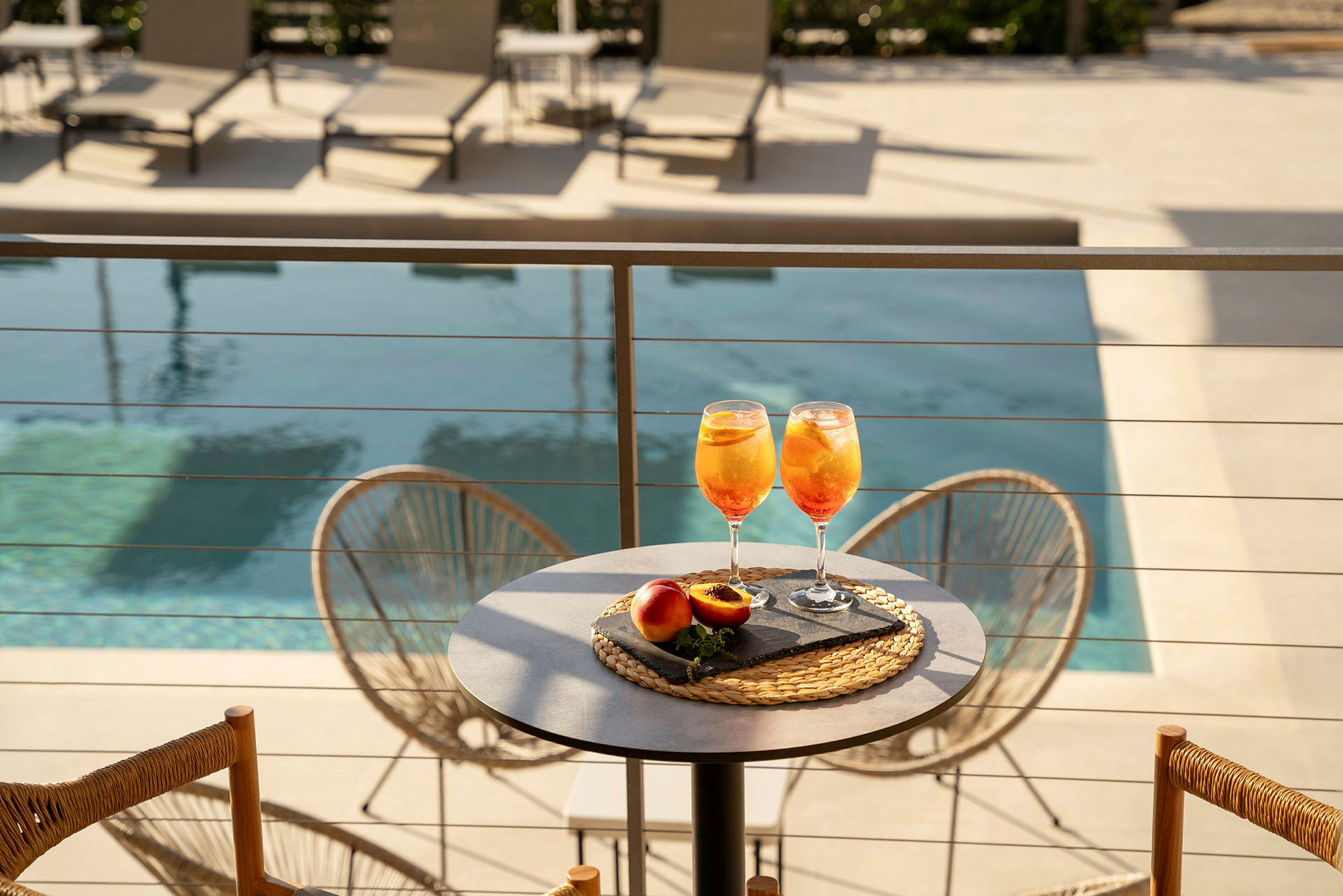 To glas med appelsindrik og ferskner er placeret på et bord nær en pool. (AI-genereret tekst)