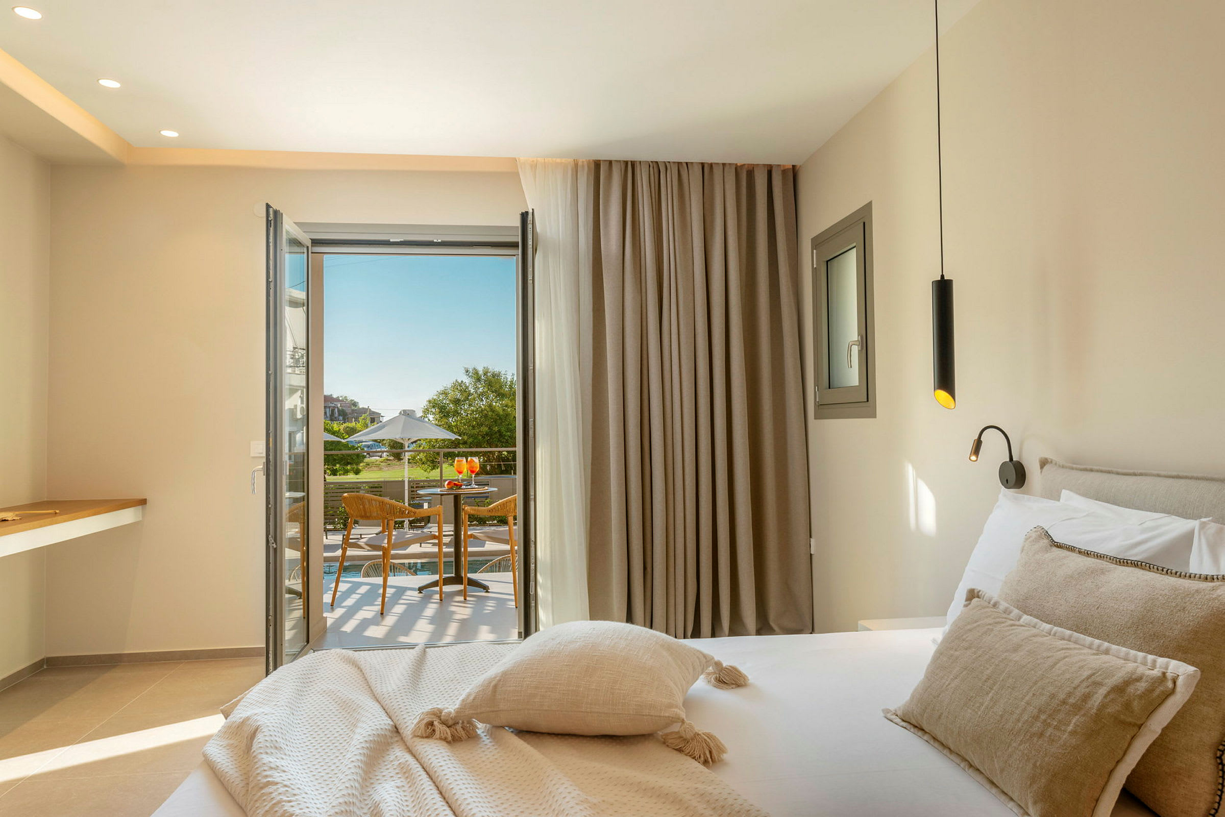 Et hotelværelse med en seng, en åben dør til en balkon med siddeområde og udsigt over grønne områder. (AI-genereret tekst)