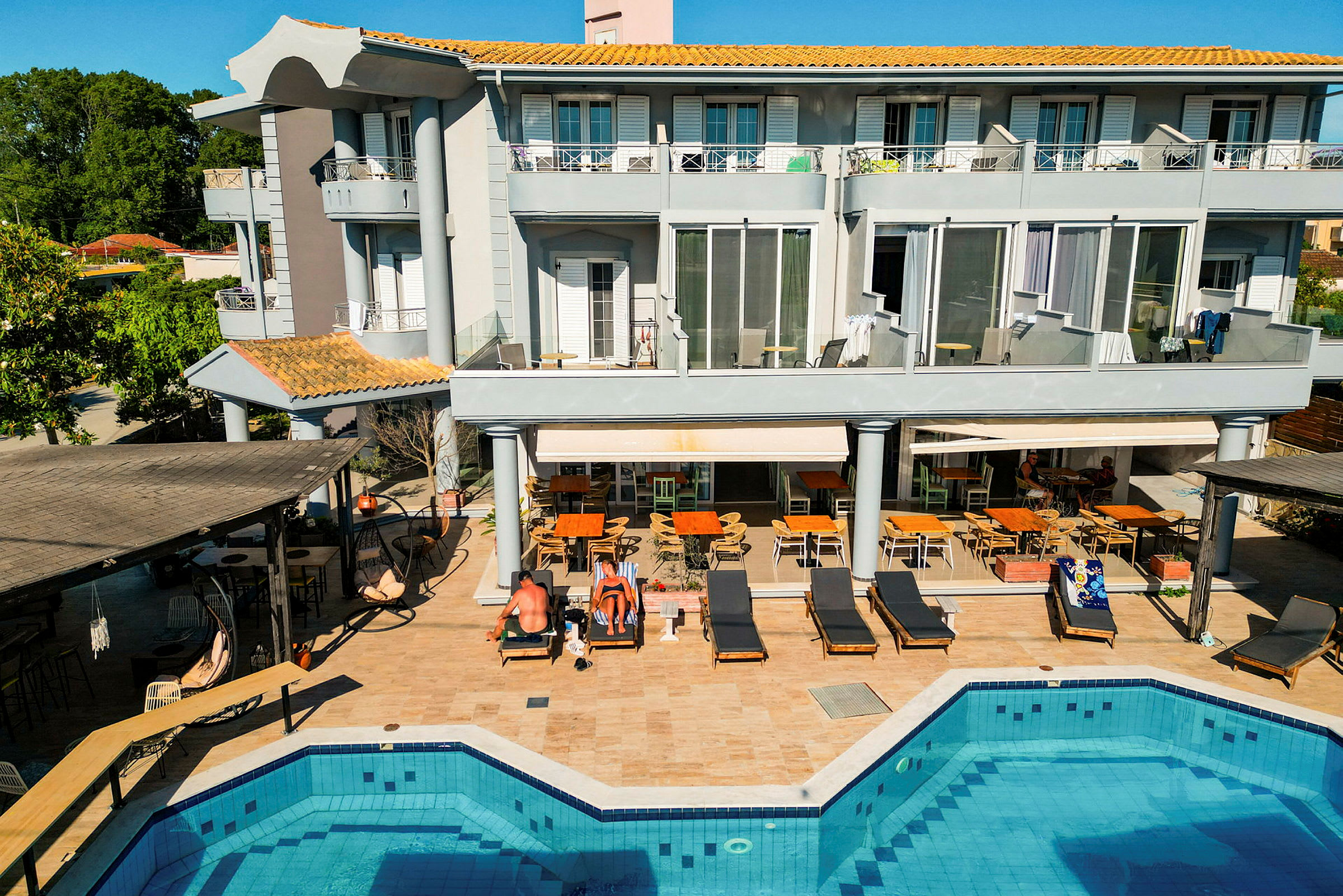 Et treetagers hotel ved en pool med omkringliggende liggestole og siddepladser. (AI-genereret tekst)