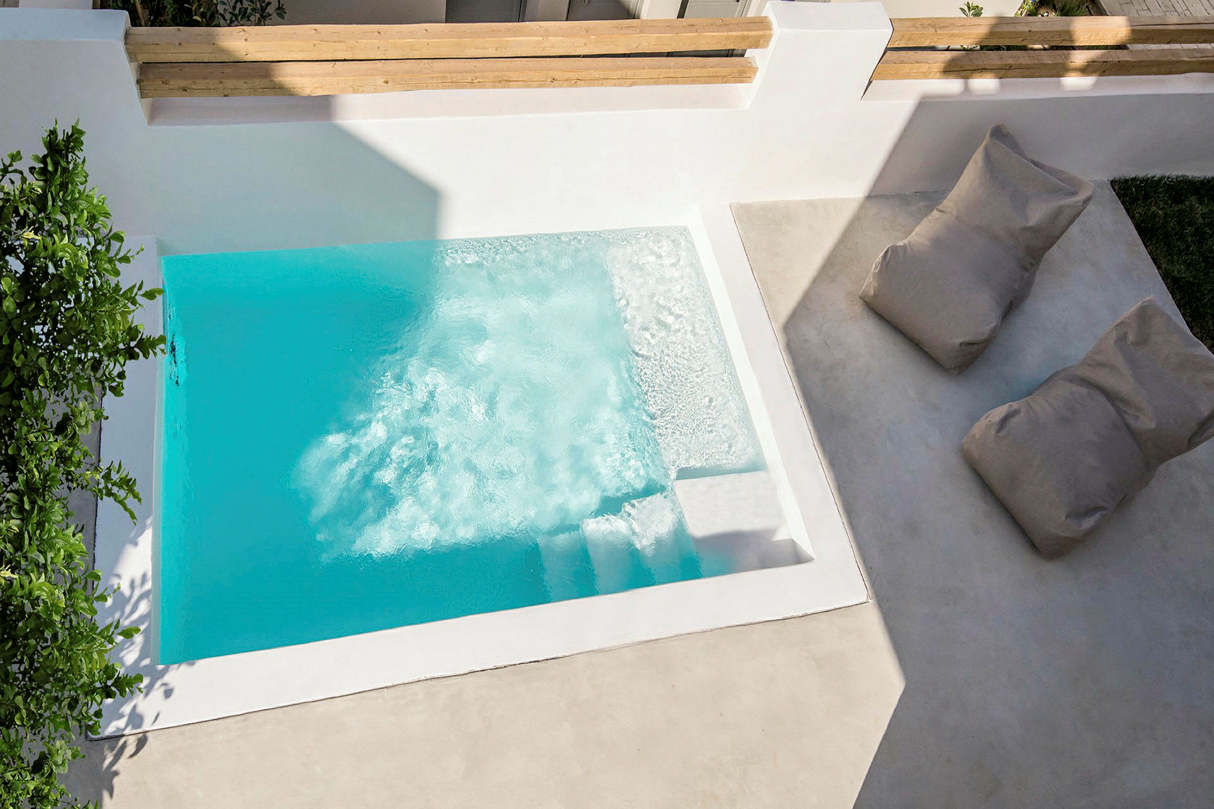 En lille pool med klart blåt vand, omgivet af hvide vægge og med to lounge-møbler ved siden af. (AI-genereret tekst)