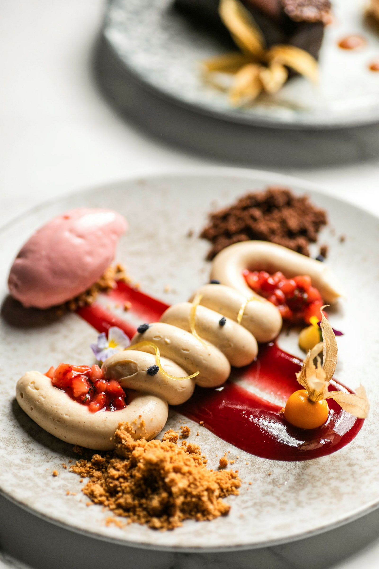 En tallerken med en elegant anrettet dessert bestående af forskellige creme- og frugtelementer. (AI-genereret tekst)