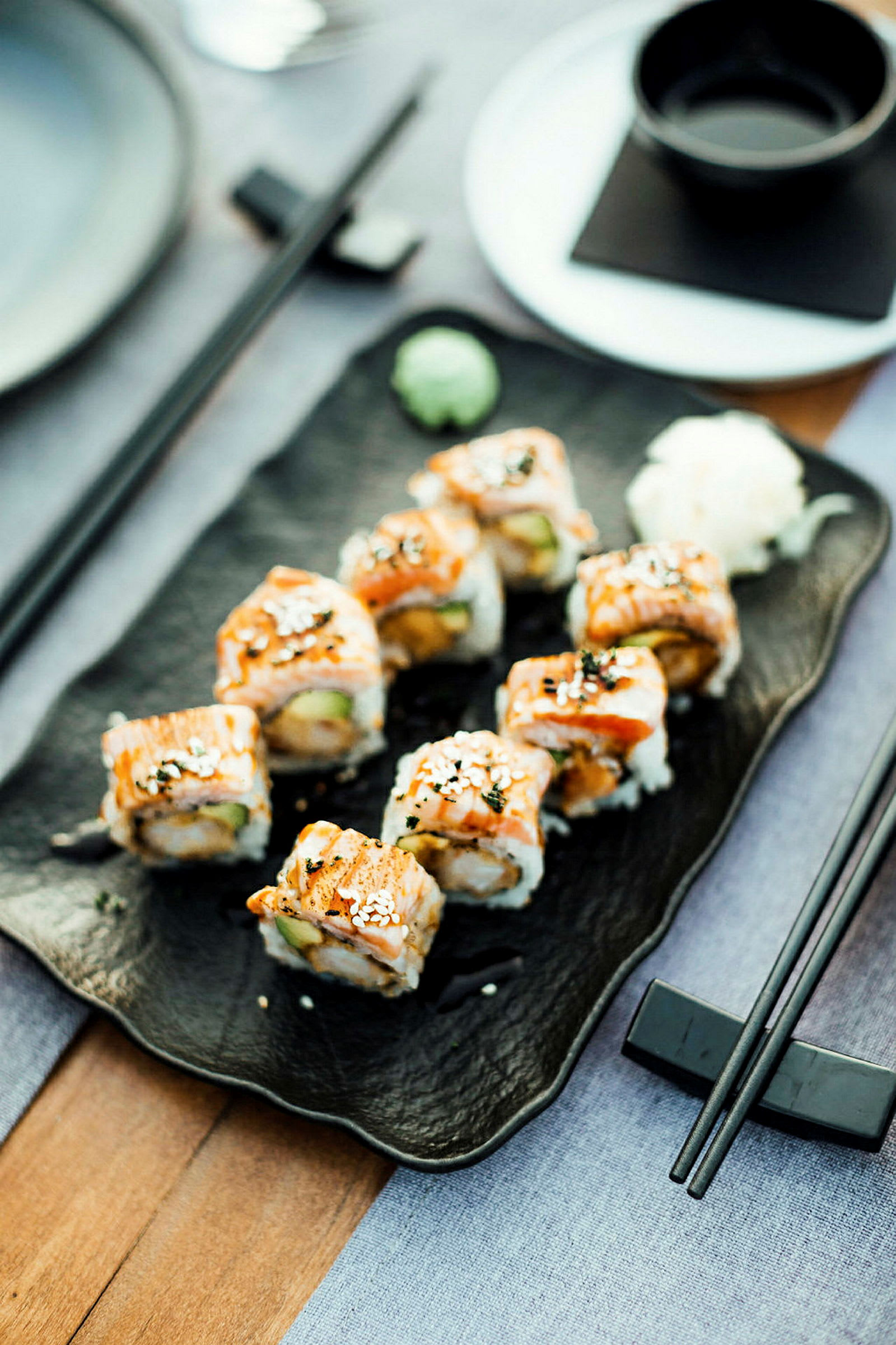 Retten viser en servering af sushi anrettet på et sort fad med dekorationer. (AI-genereret tekst)