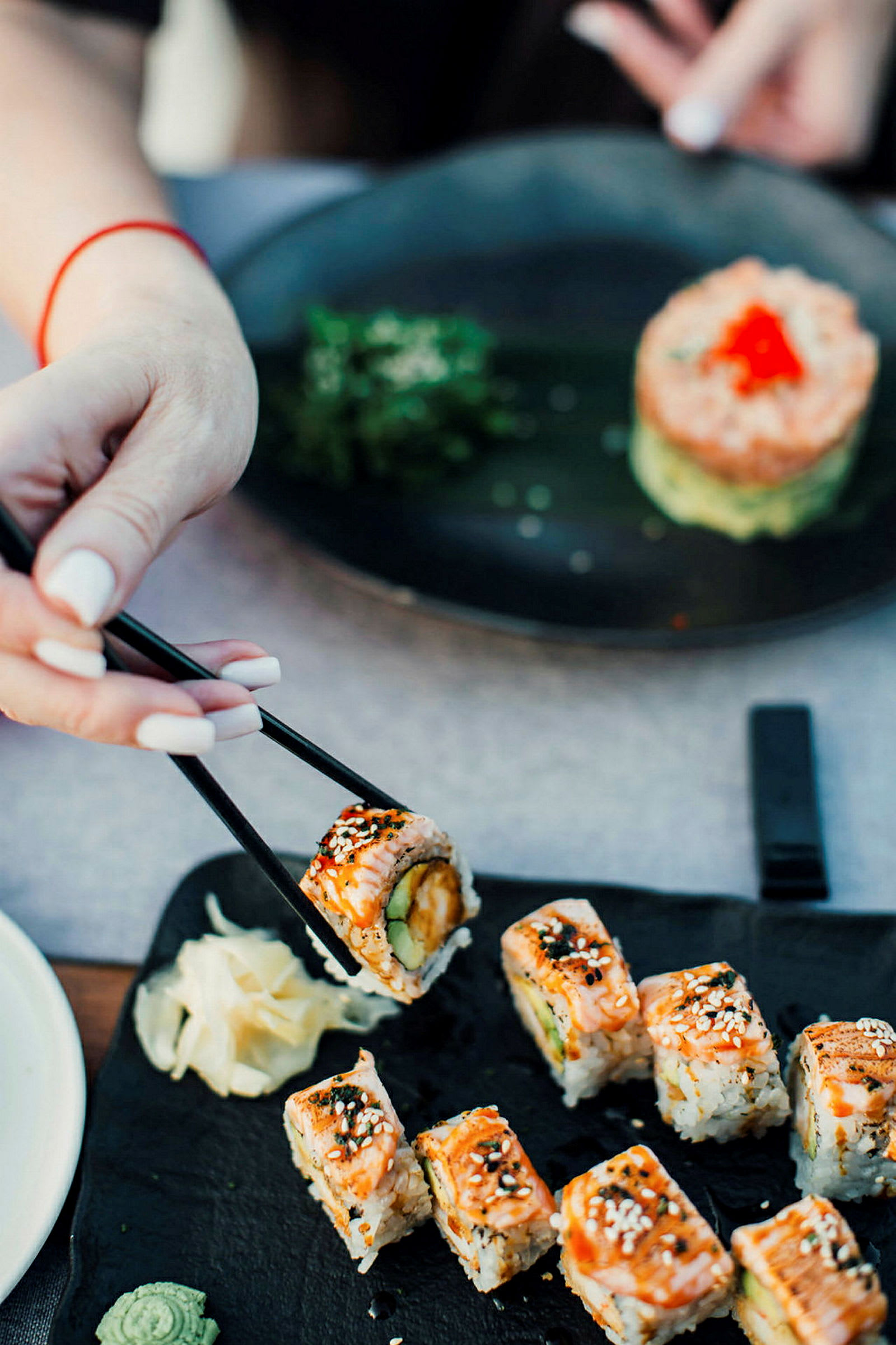 Sushi serveret på en sort tallerken, med en hånd der holder et stykke med spisepinde. (AI-genereret tekst)