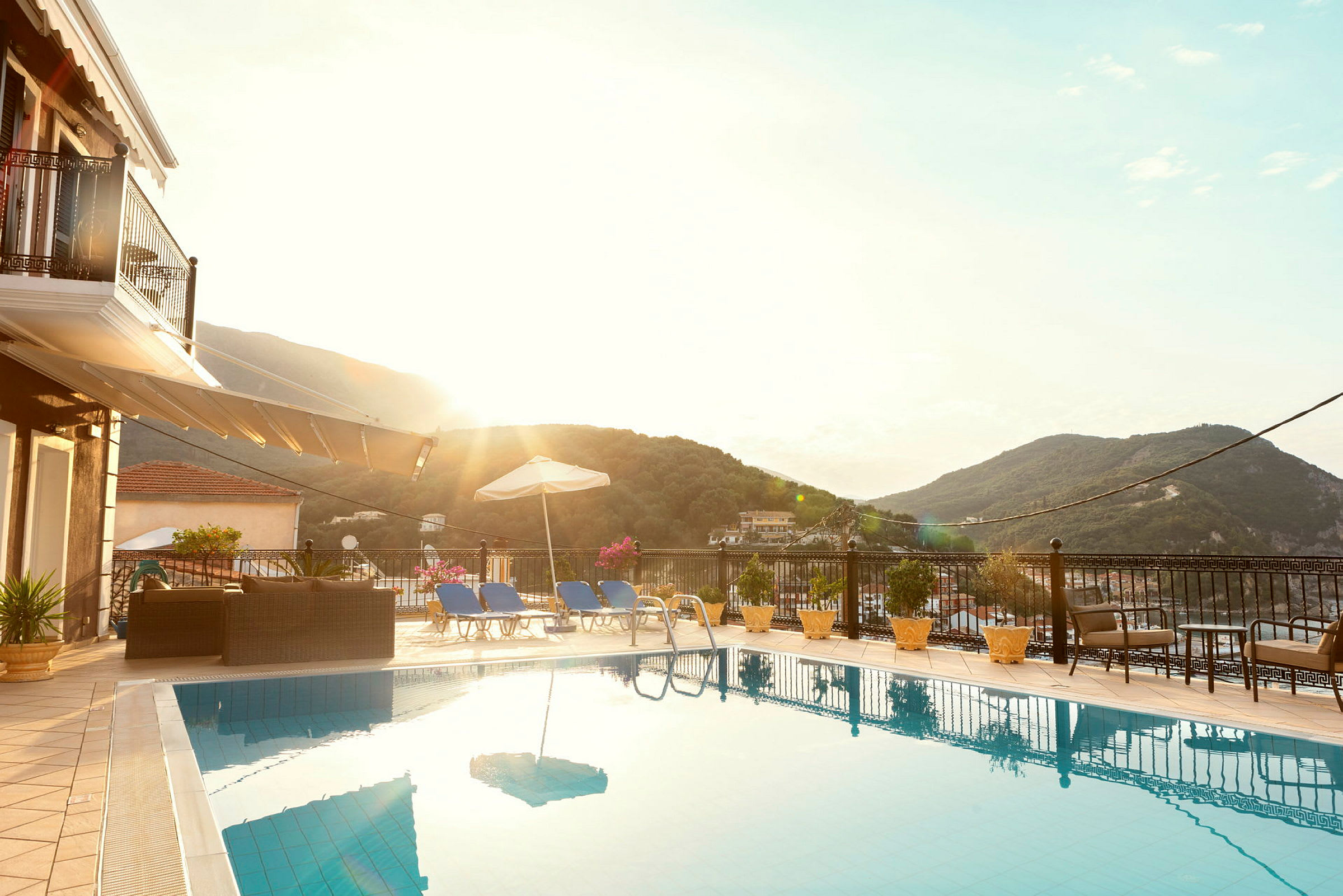 Udendørs pool med liggestole og parasol, omgivet af frodige bjerge. (AI-genereret tekst)