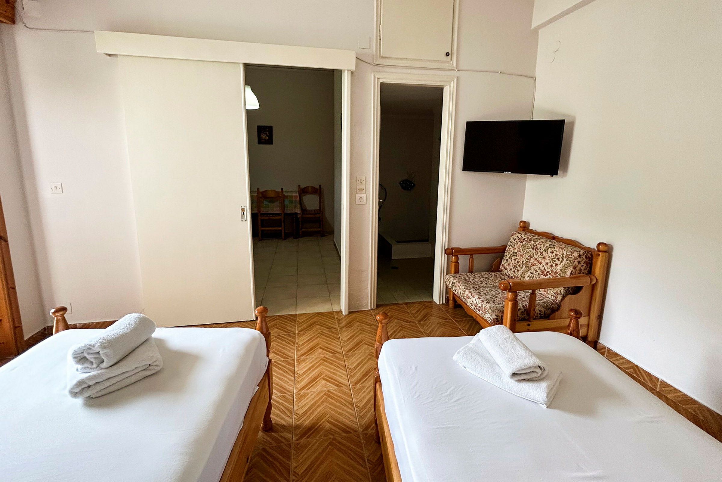 Et hotelværelse med to senge, et lukket skab, en lille siddeplads og et TV på væggen. (AI-genereret tekst)