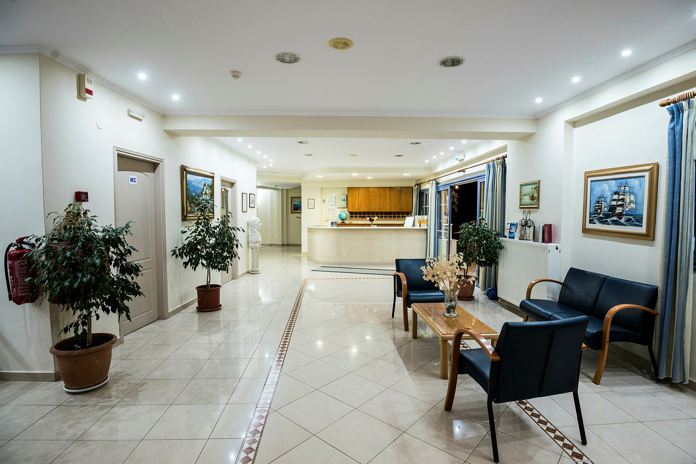 Billede af en hotellobby med reception, siddeområde og dekorative planter. (AI-genereret tekst)