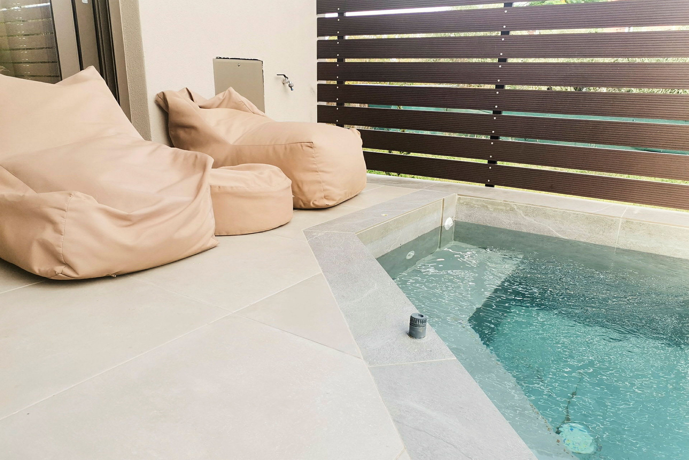 To beige sækkestole ved siden af en lille pool på en terrasse. (AI-genereret tekst)