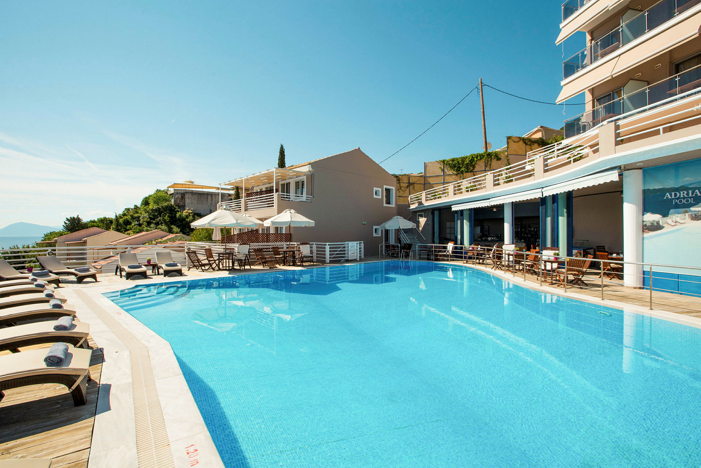 Billede af en udendørs pool med liggestole og parasoller ved et hotel. (AI-genereret tekst)
