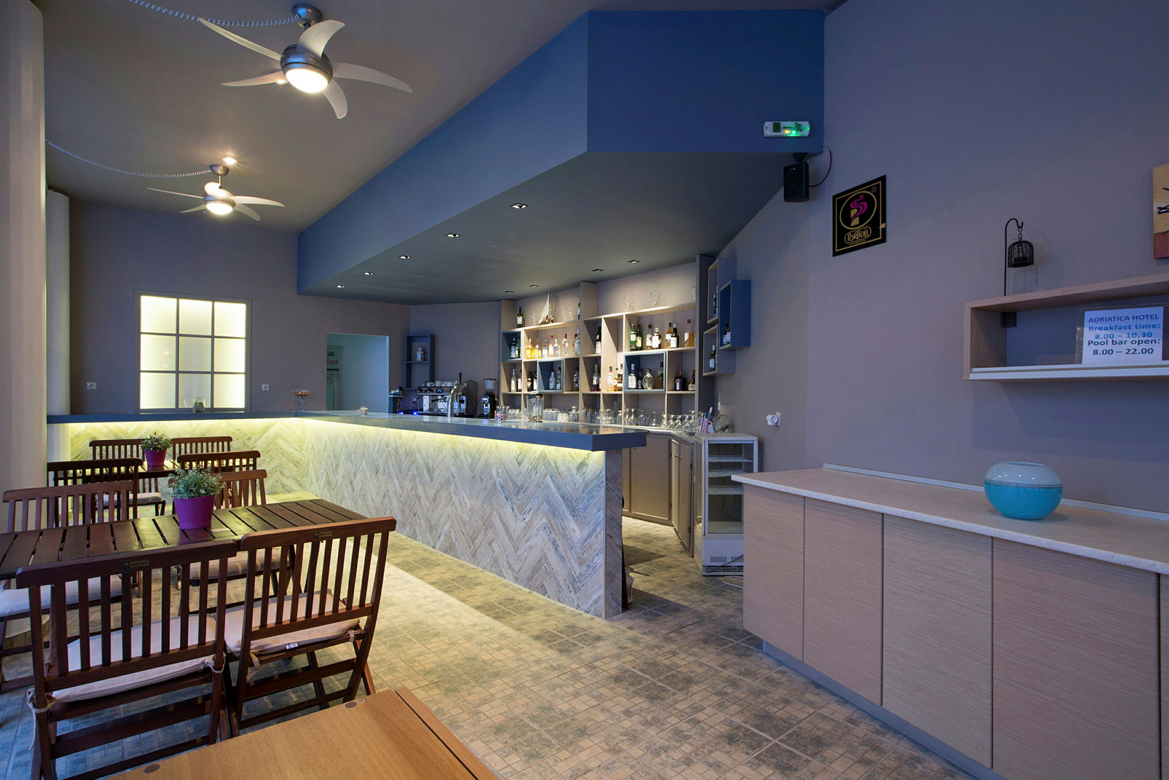 En interiørudsigt af en hotelbar med træborde og stole samt en oplyst bar. (AI-genereret tekst)