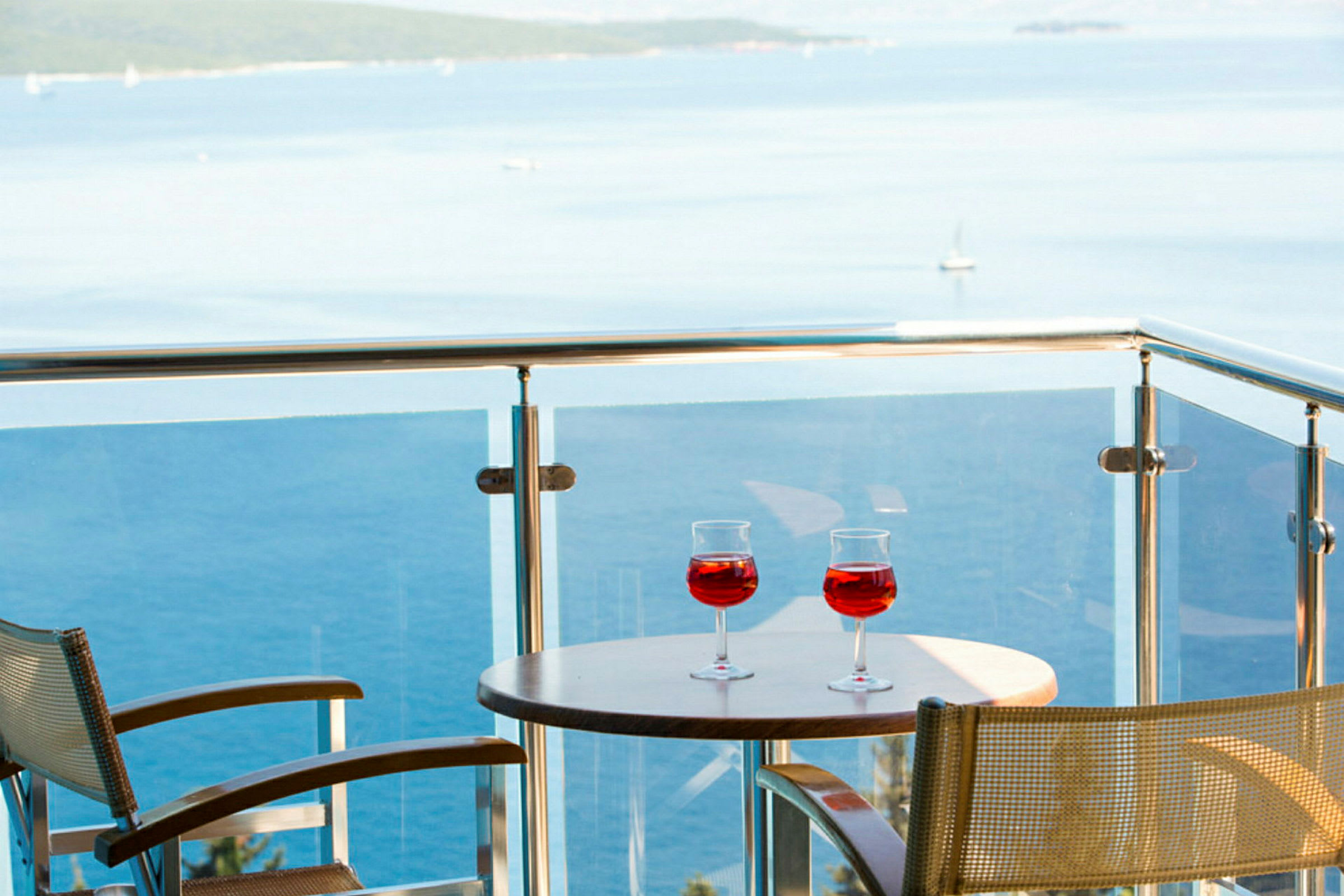 To glas med rød drik på et bord på en altan med udsigt over havet. (AI-genereret tekst)