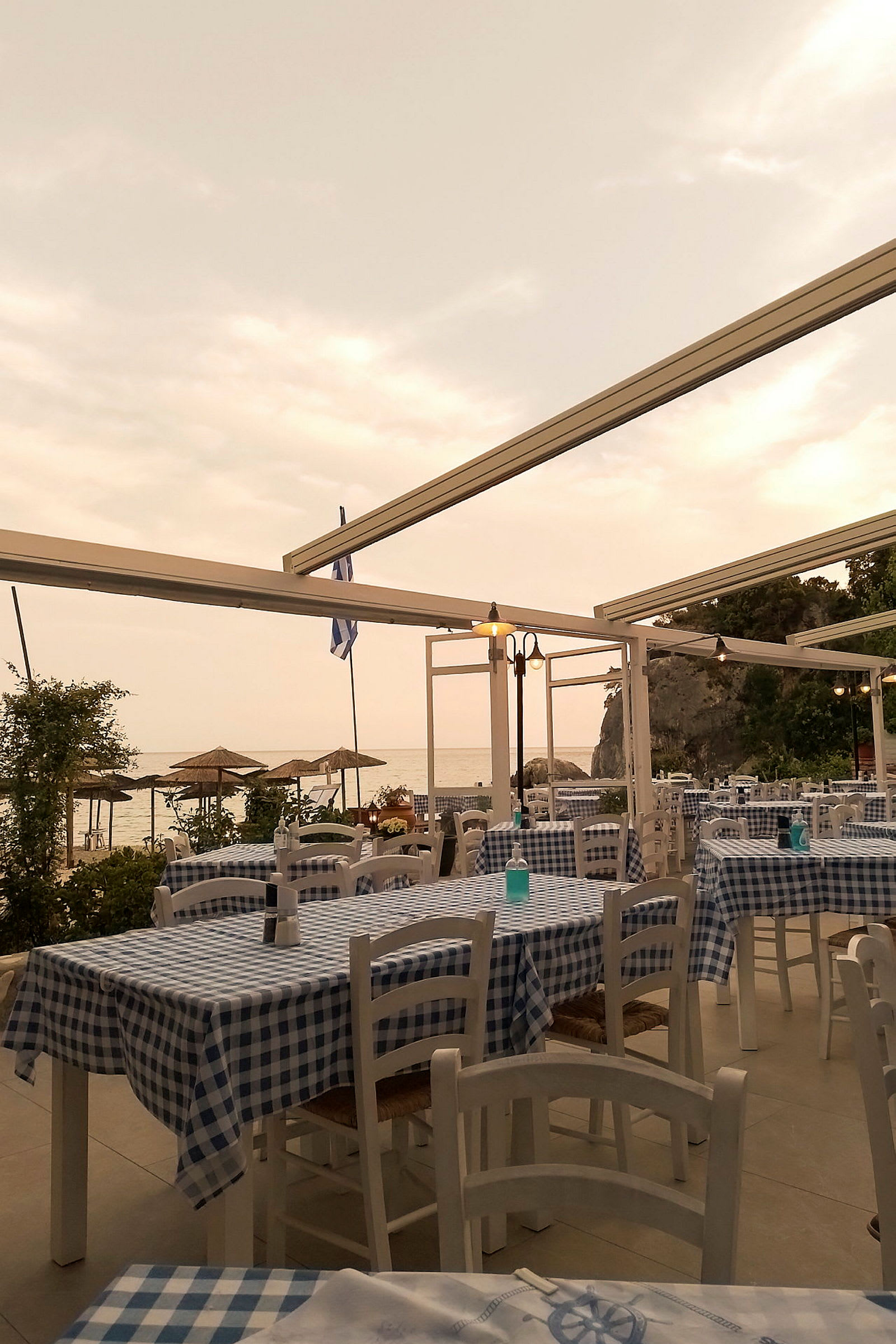 Restaurant med ternede duge og havudsigt under overskyet himmel. (AI-genereret tekst)