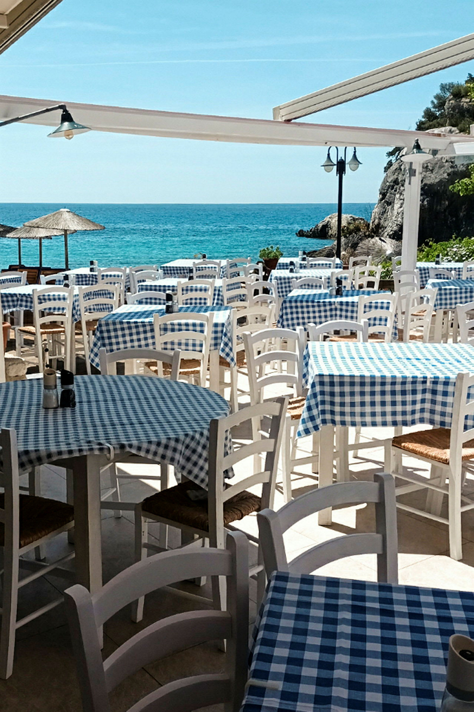 Restaurant ved havet med dækkede borde og stole udendørs. (AI-genereret tekst)